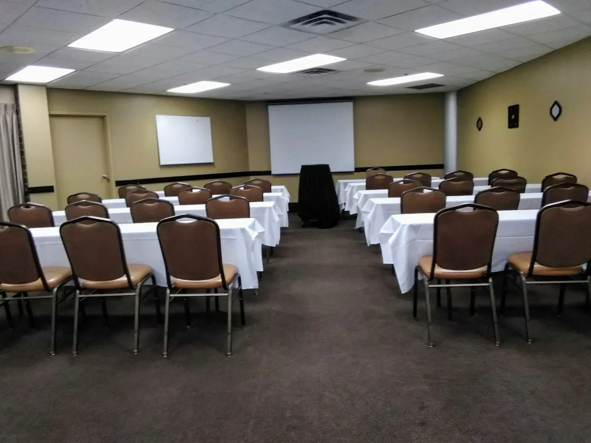 Conference room with rows of brown chairs and white-clothed tables facing projection screens.