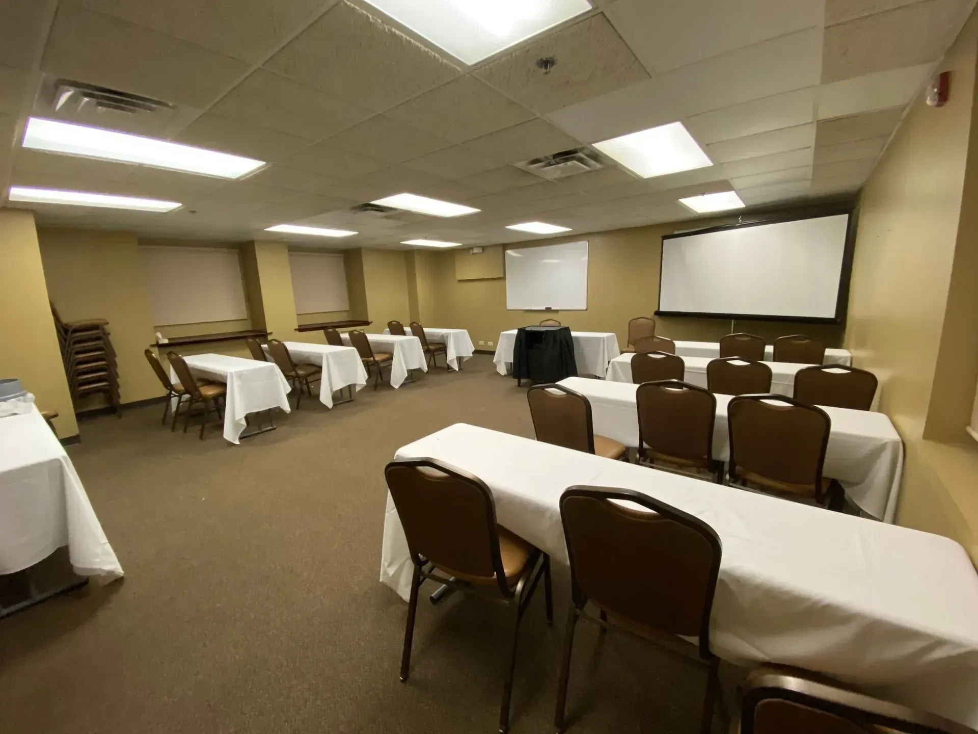 Empty conference room with tables covered in white cloths and rows of brown chairs, plus projection screens on the front wall
