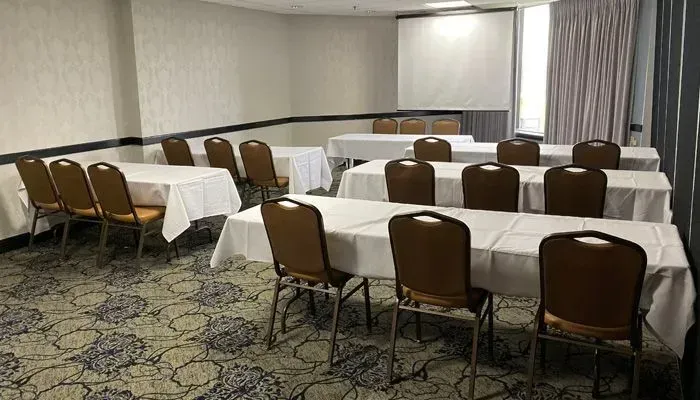 Empty conference room with rows of tables covered in white cloths and brown chairs on patterned carpet