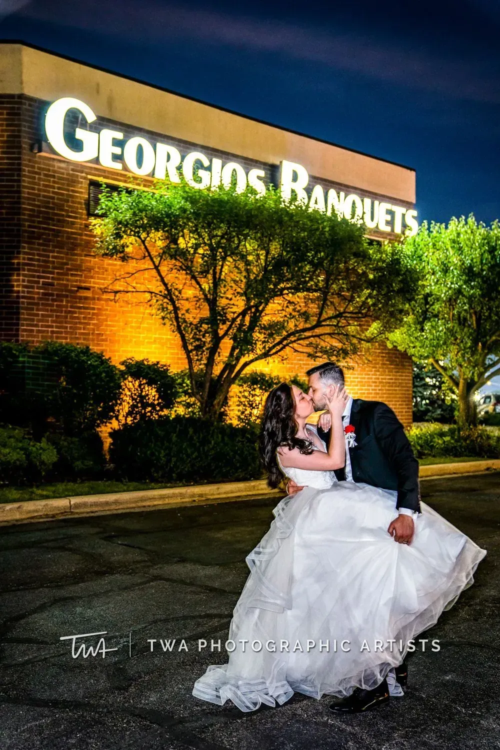 Bride and groom kissing in front of Georgios Banquets at night