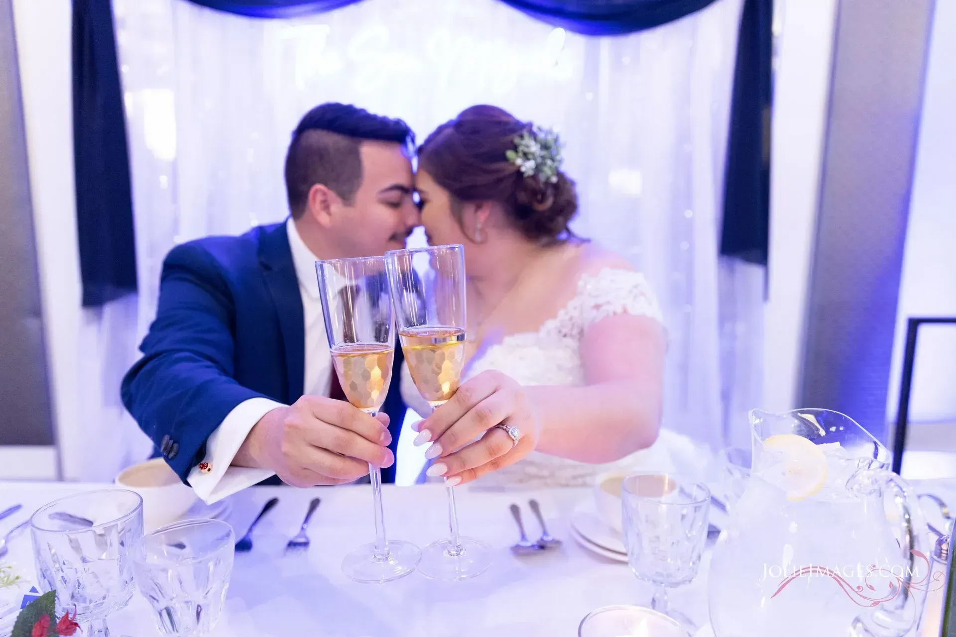 Couple toasting champagne at a wedding reception table, under soft purple lighting