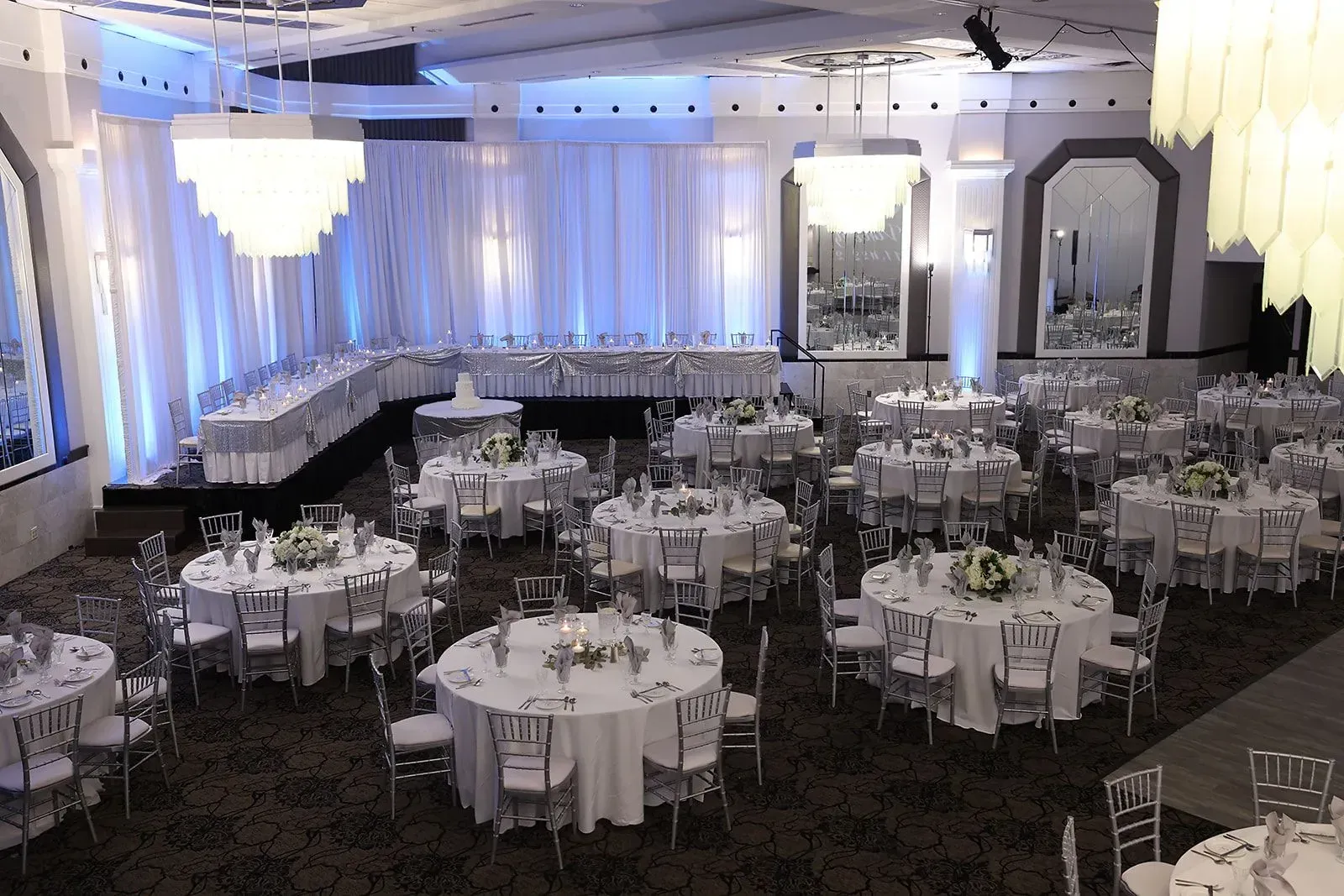 Elegant banquet hall set with round tables, white linens, and chandeliers before an event