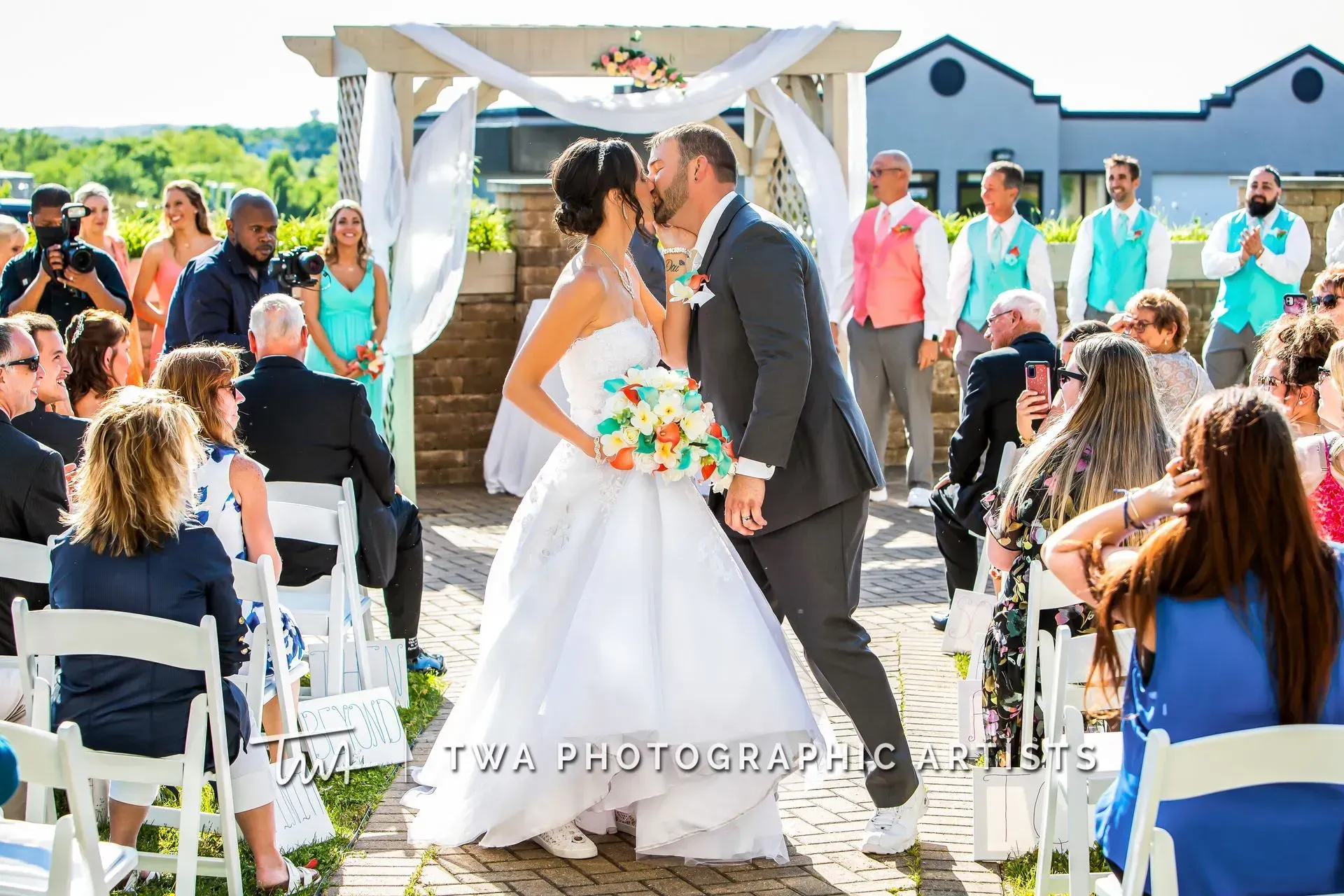 Bride and groom kiss at an outdoor wedding ceremony with guests seated nearby