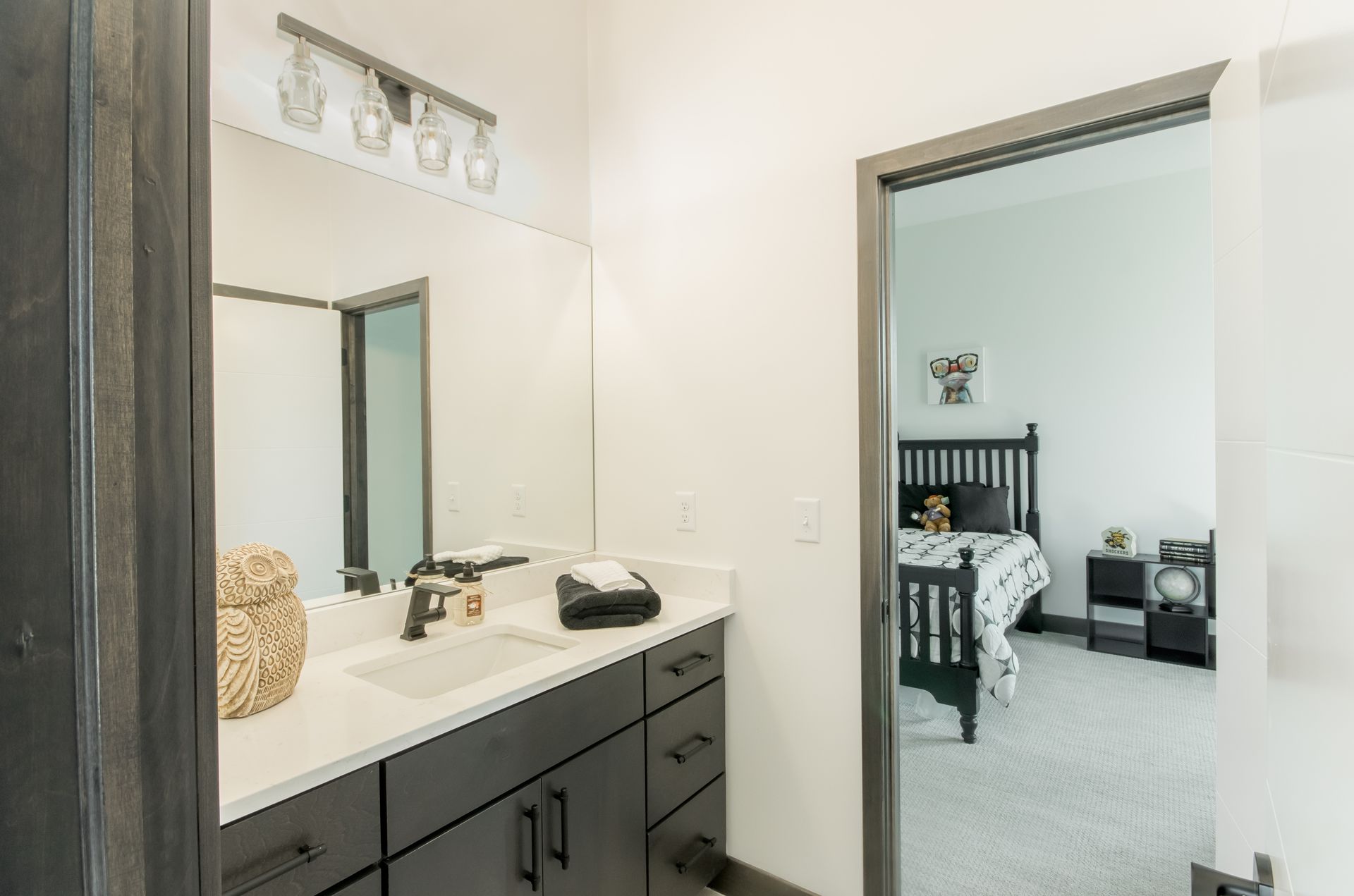 A bathroom with a sink and a mirror and a bedroom in the background.