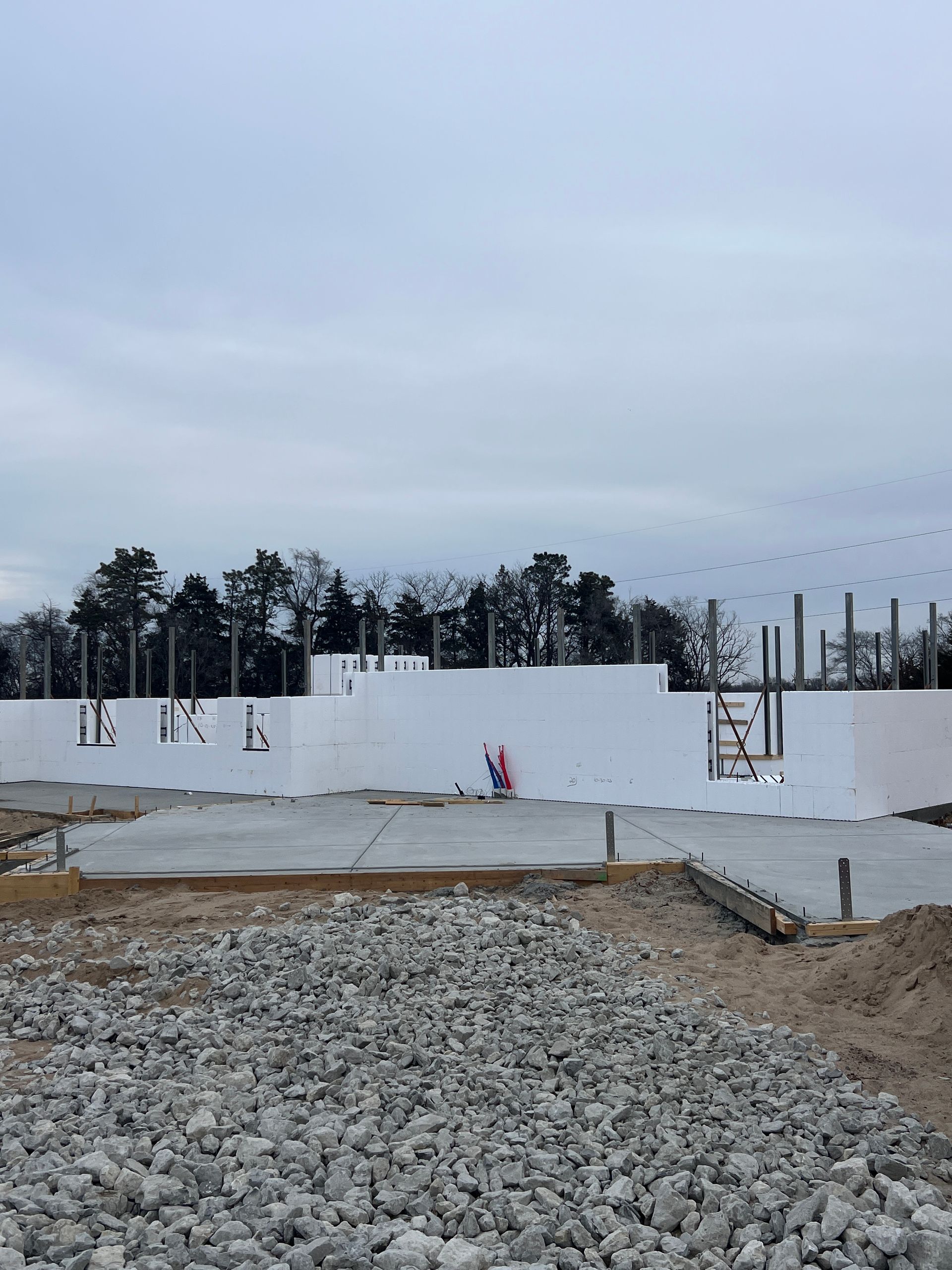 Construction site with concrete foundation and white insulated concrete forms, cloudy sky.