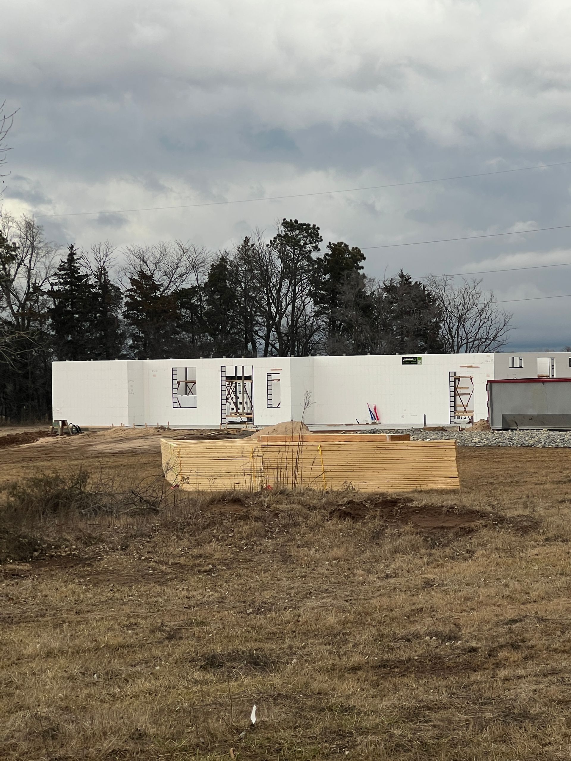 Construction of a white, rectangular building with windows under a cloudy sky. Wooden beams are in front.