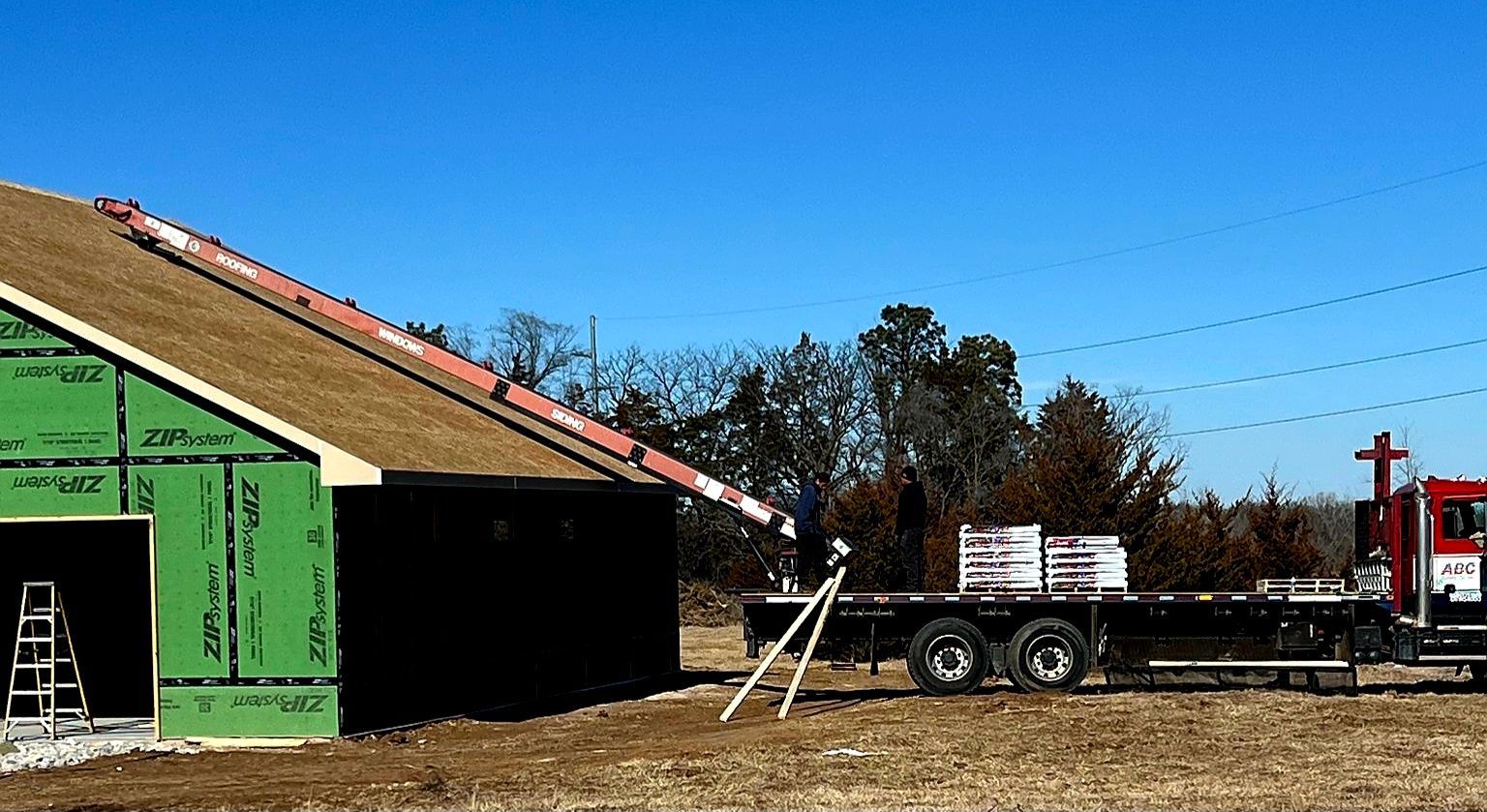 Construction site with a truck unloading roofing materials onto a partially built structure, sunny day.