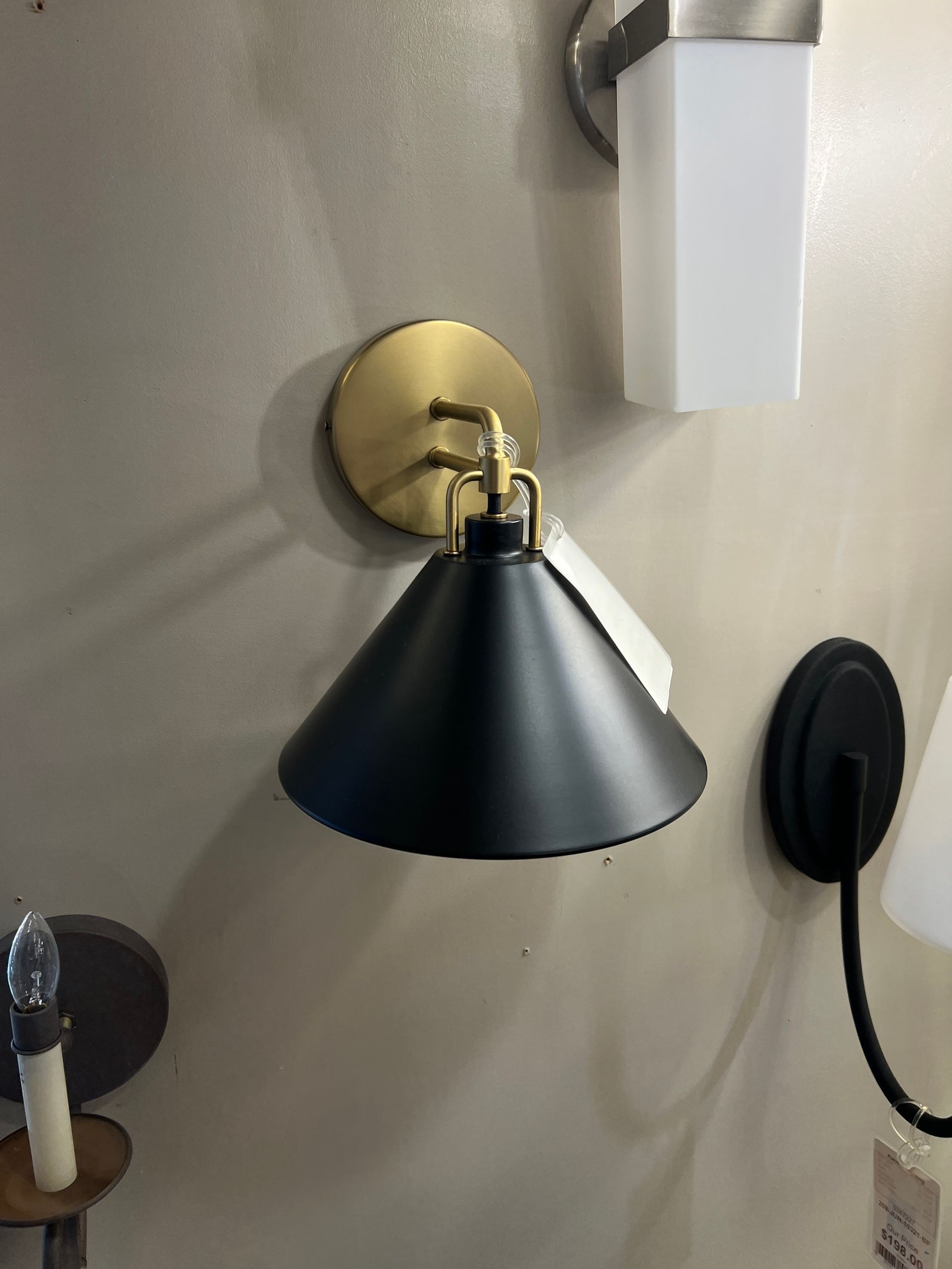 Black conical wall-mounted lamp with gold-toned hardware, on a tan wall.