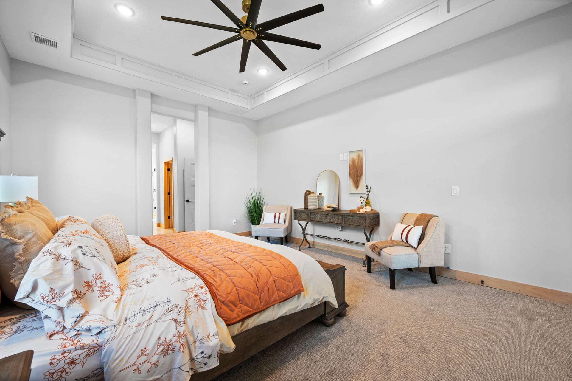 A bedroom with a bed, chairs, and a ceiling fan.