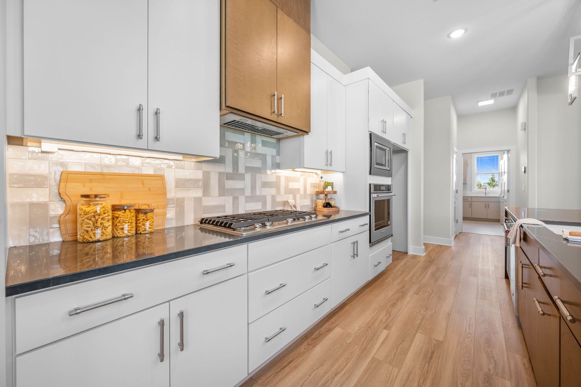 A kitchen with white cabinets and wooden floors and a stove top oven.