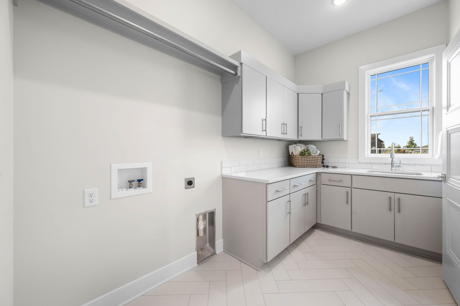A laundry room with white cabinets, a sink, and a window.