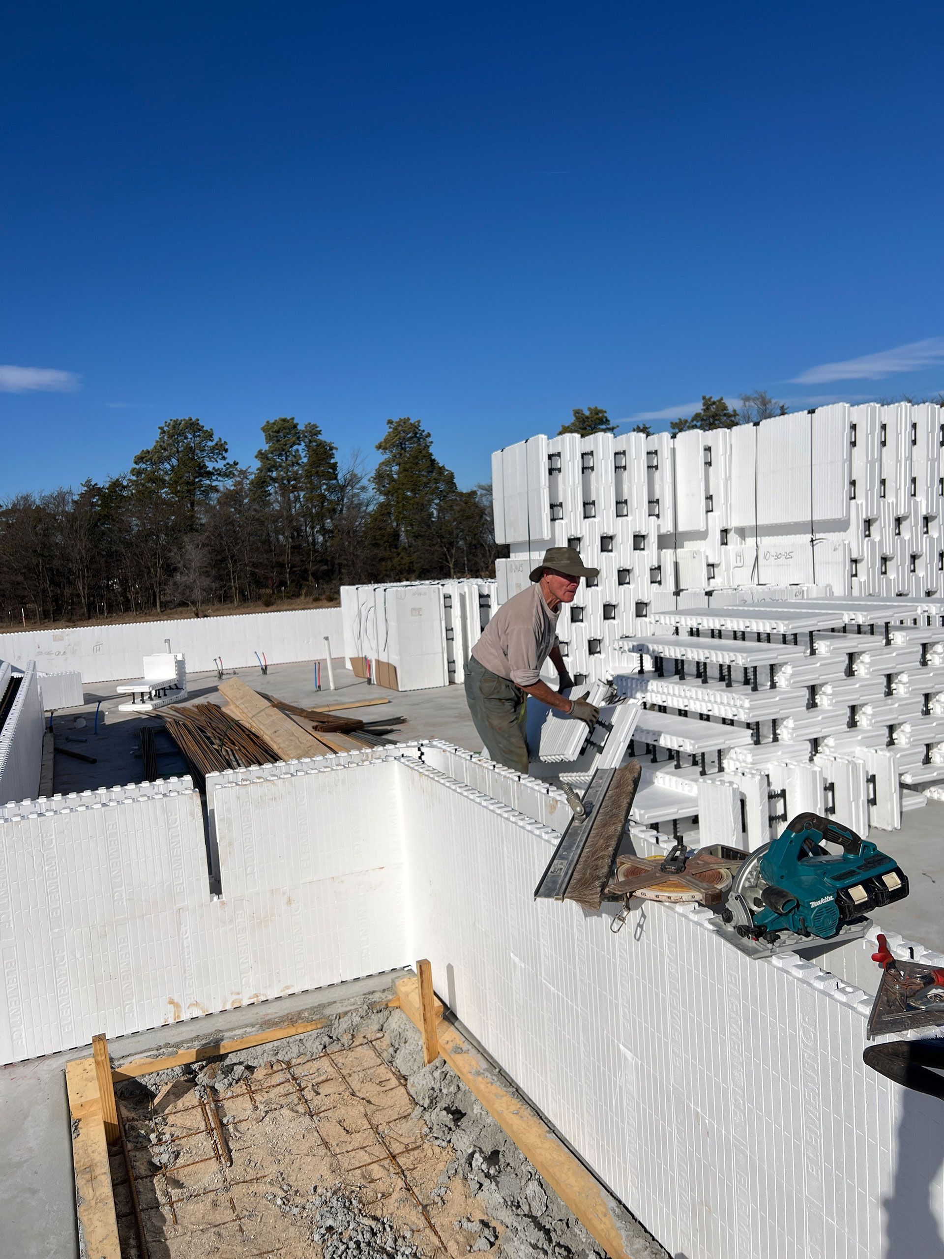 Construction worker cutting blocks on a building site. White foam blocks and blue sky visible.