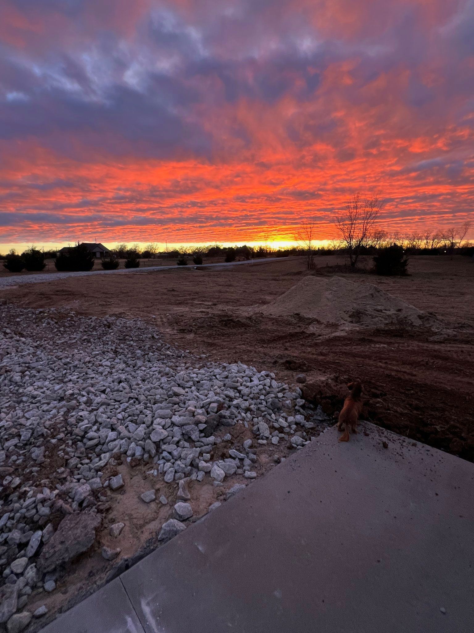 Fiery sunset over a dusty, gravel-strewn field. Concrete pad in the foreground.
