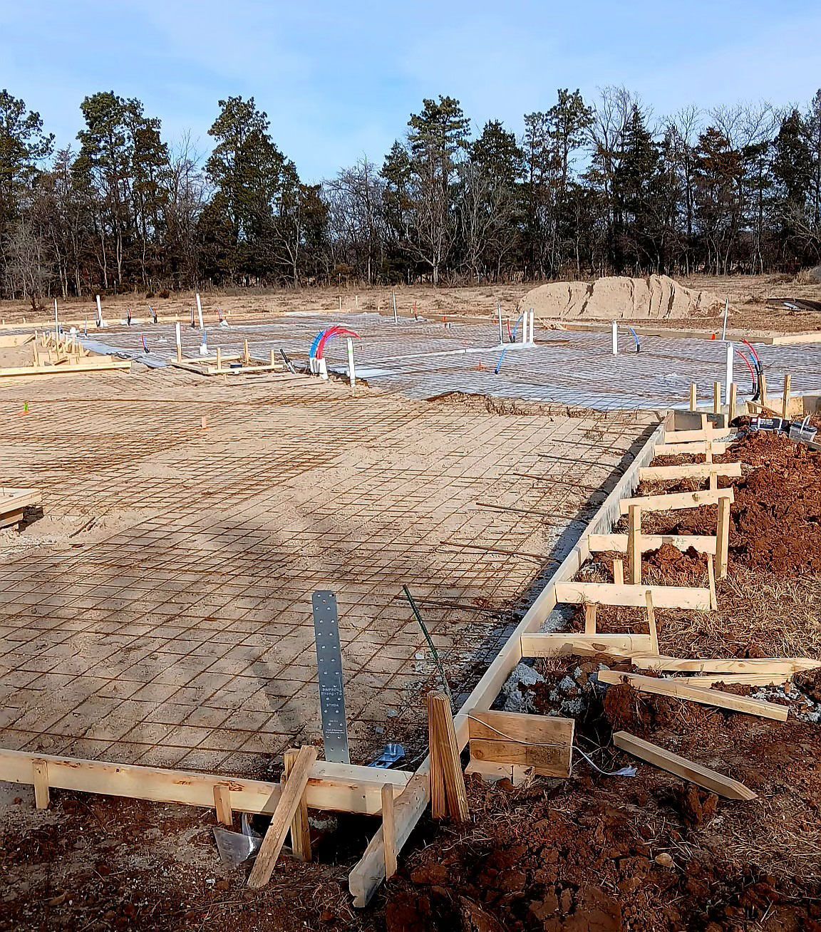 Construction site with wooden forms, rebar, and plumbing, prepared for a concrete foundation.