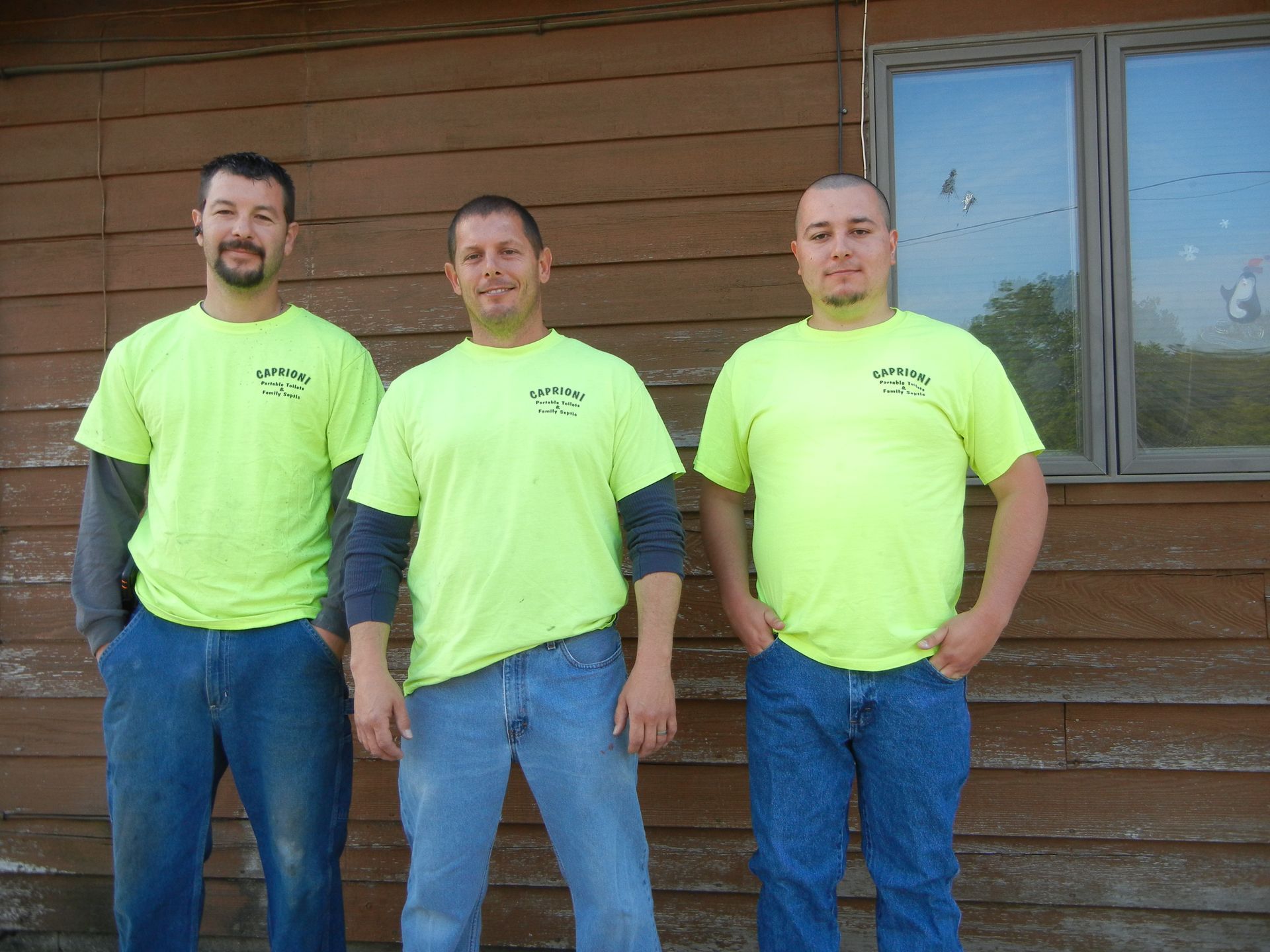 three men wearing neon yellow shirts stand in front of a wooden wall
