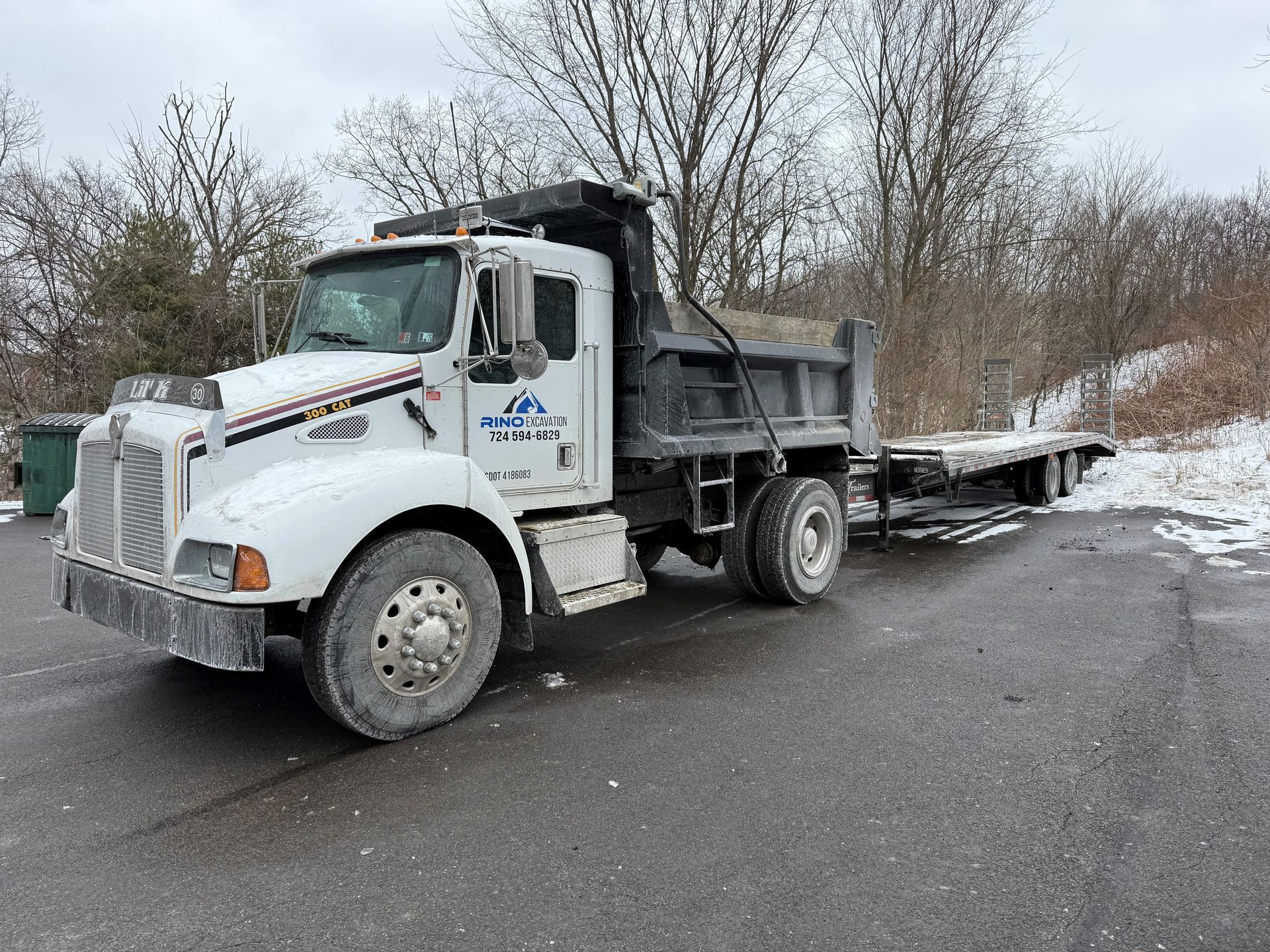 A white dump truck with a flatbed trailer attached to it is parked on the side of the road.