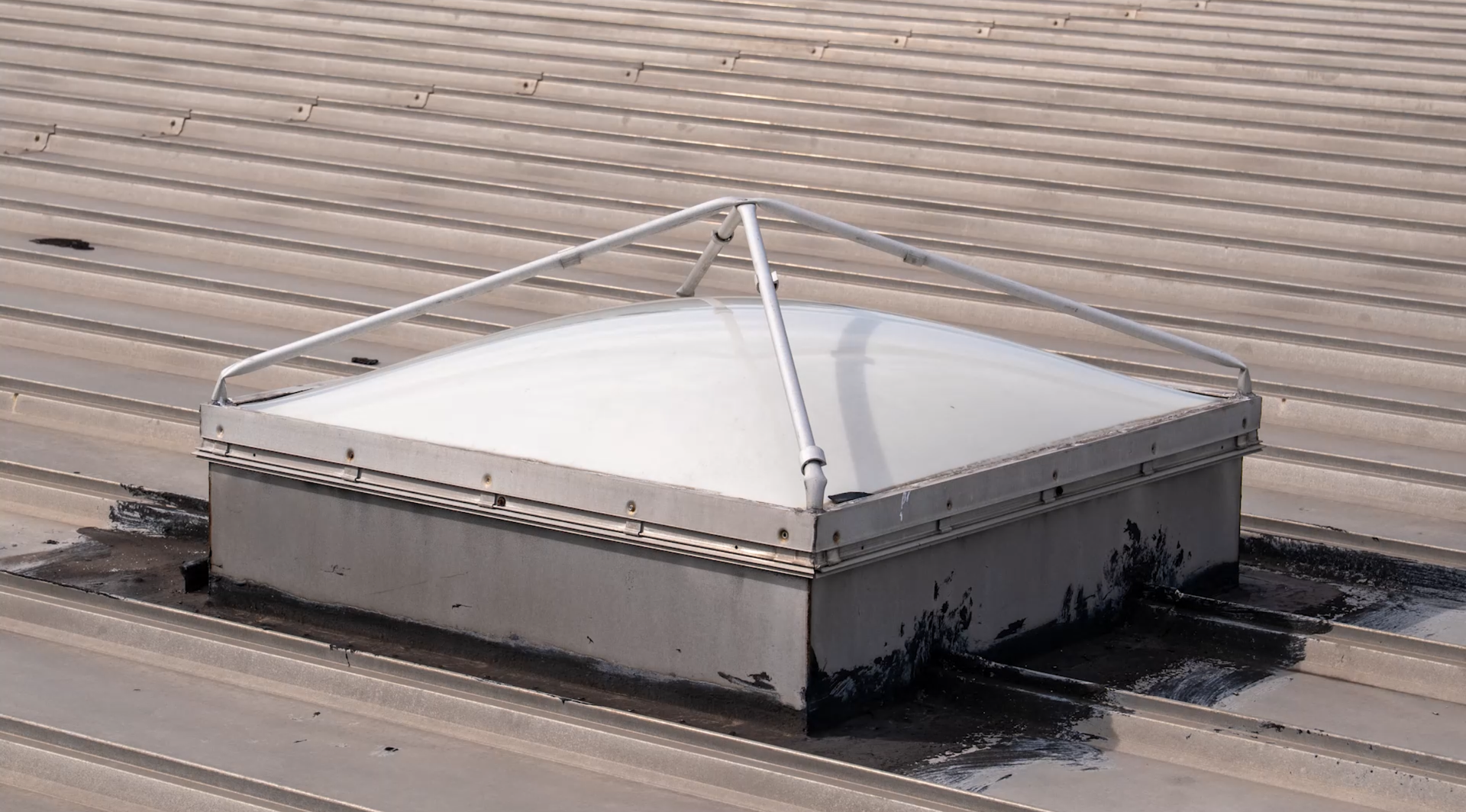 Rooftop access hatch with white metal cover and tension rods on a corrugated roof