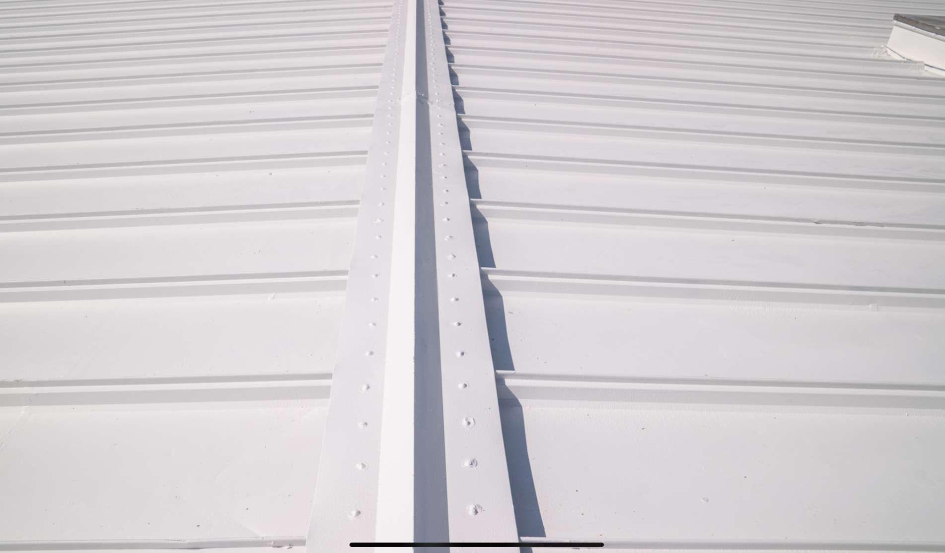 White corrugated metal roof with a central ridge seam and rows of fasteners