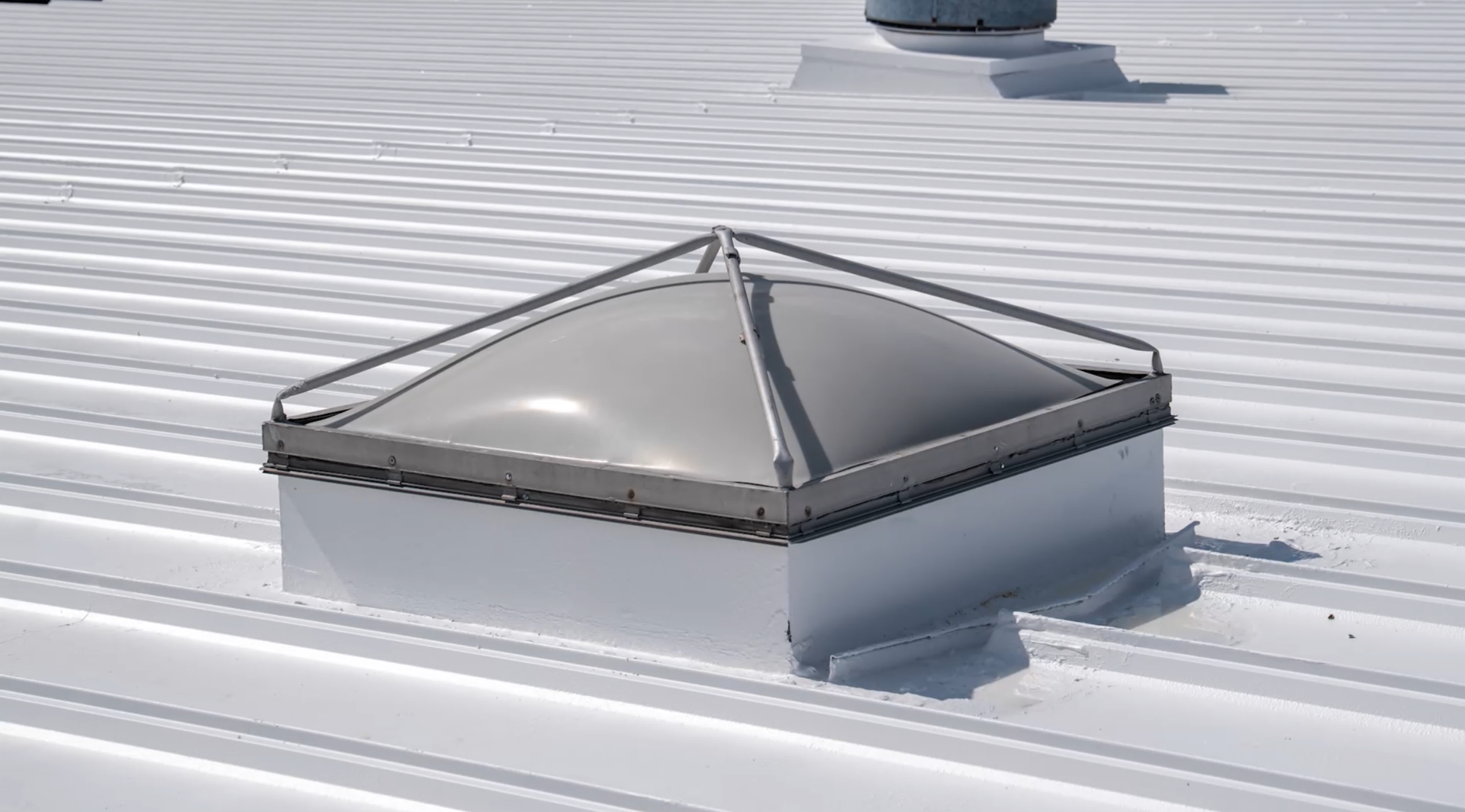 Small rooftop skylight with a metal frame on a white, snow-covered roof