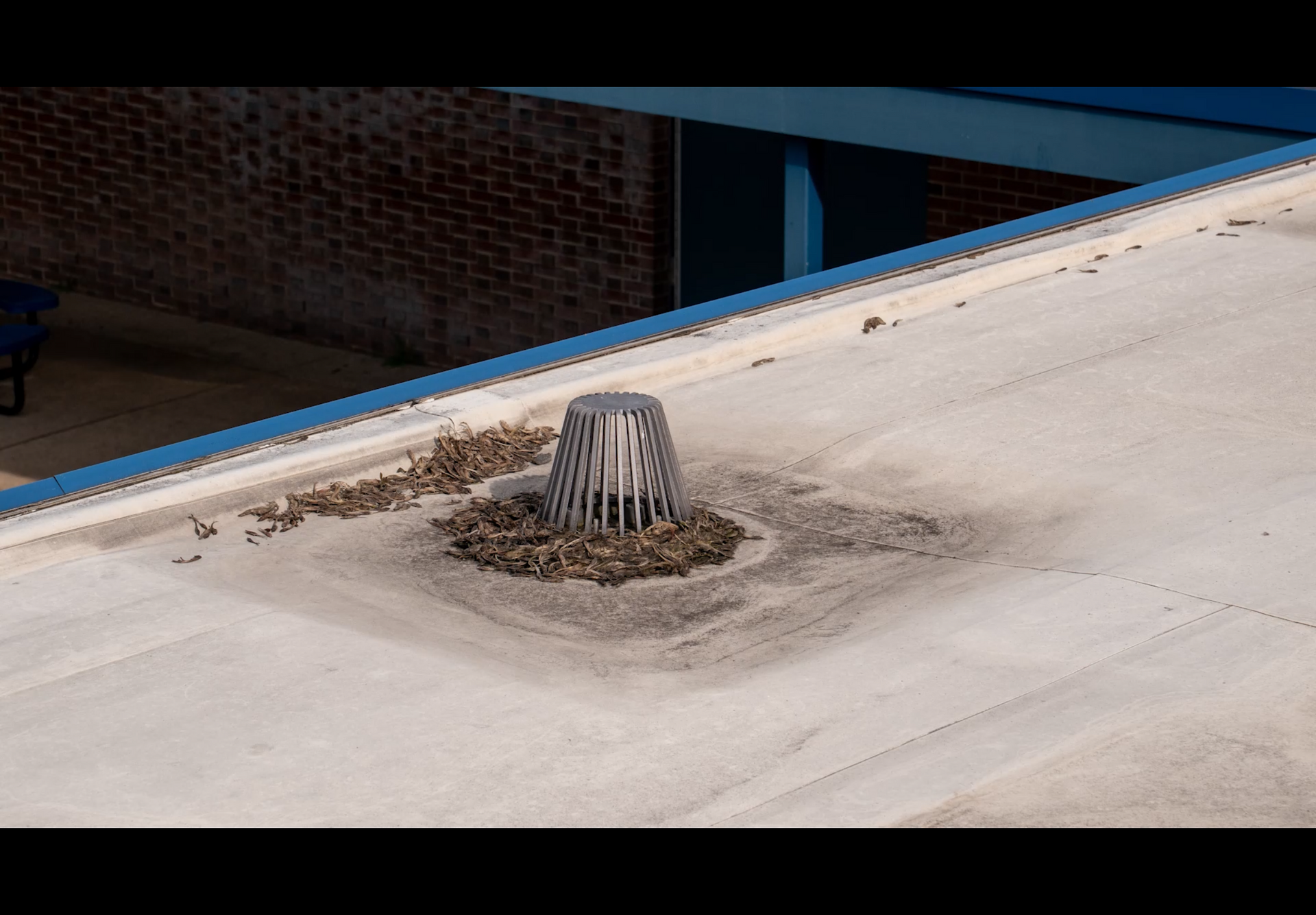 Rooftop vent capped with a metal cover on a light concrete roof near a brick wall.