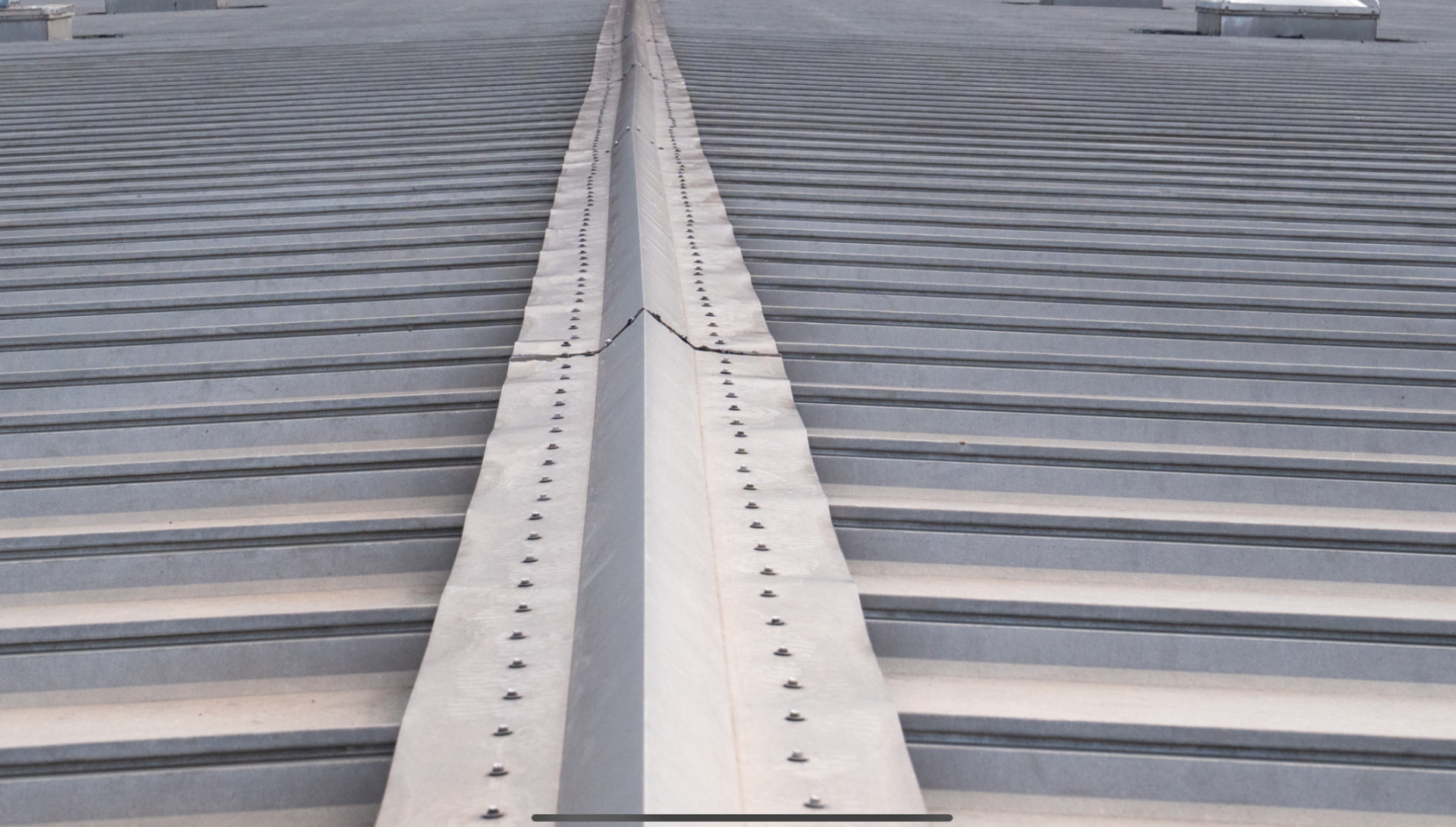 Close-up of a metal rooftop seam with rows of gray corrugated panels on both sides.