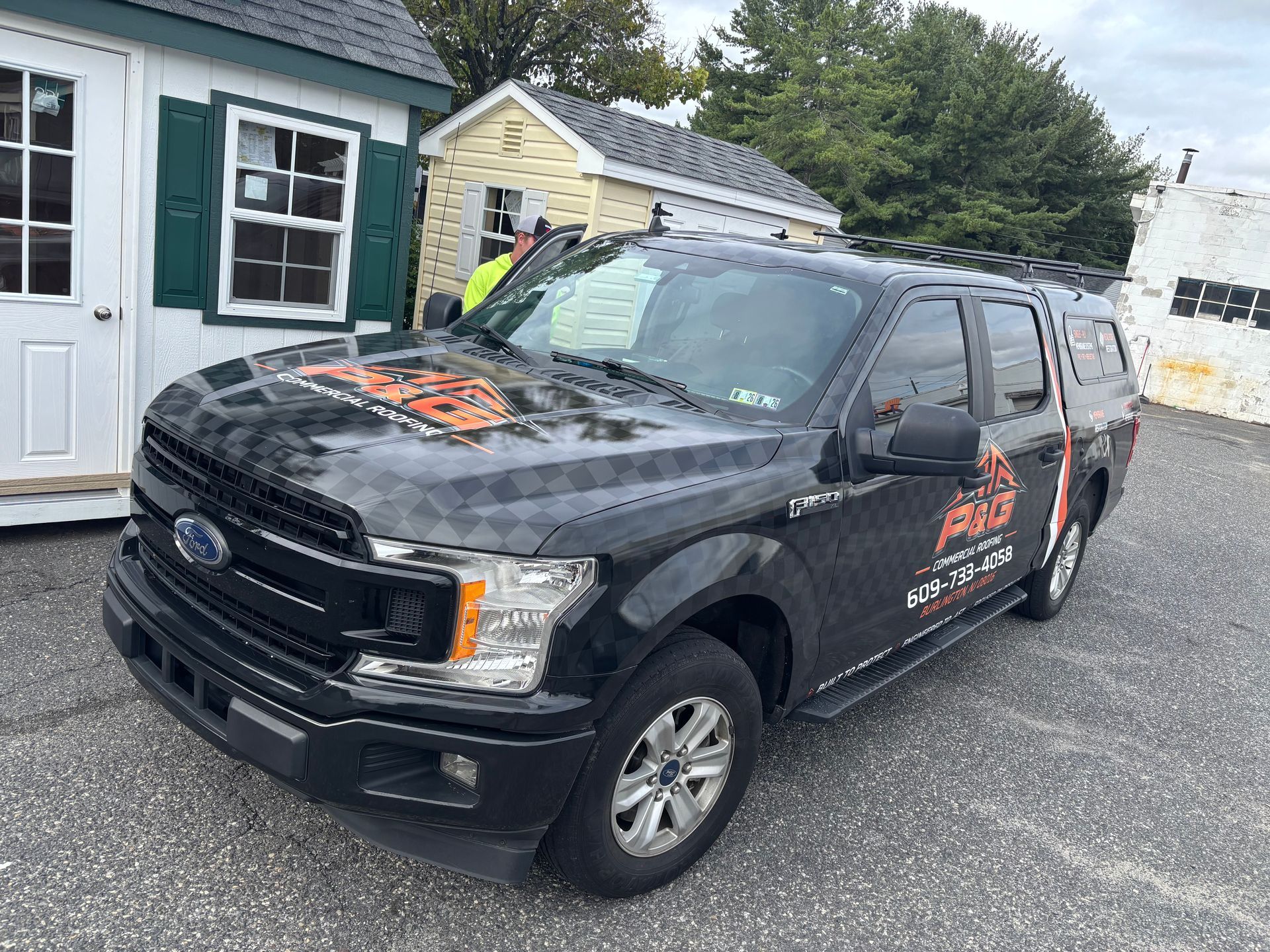 Black Ford pickup truck with orange lettering parked on a gravel lot beside small buildings