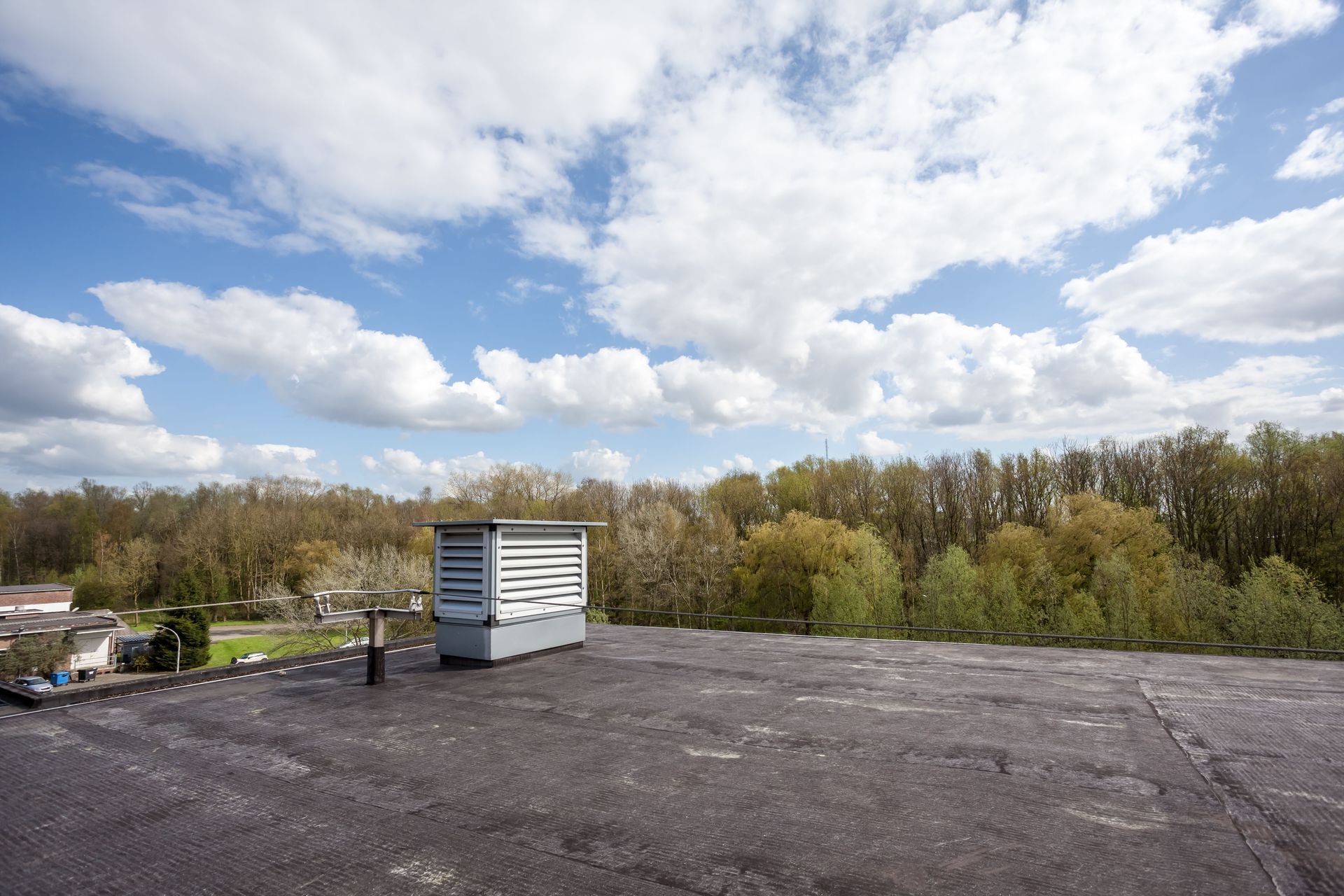 Weather station on a flat roof, blue sky with puffy clouds, trees in the background.