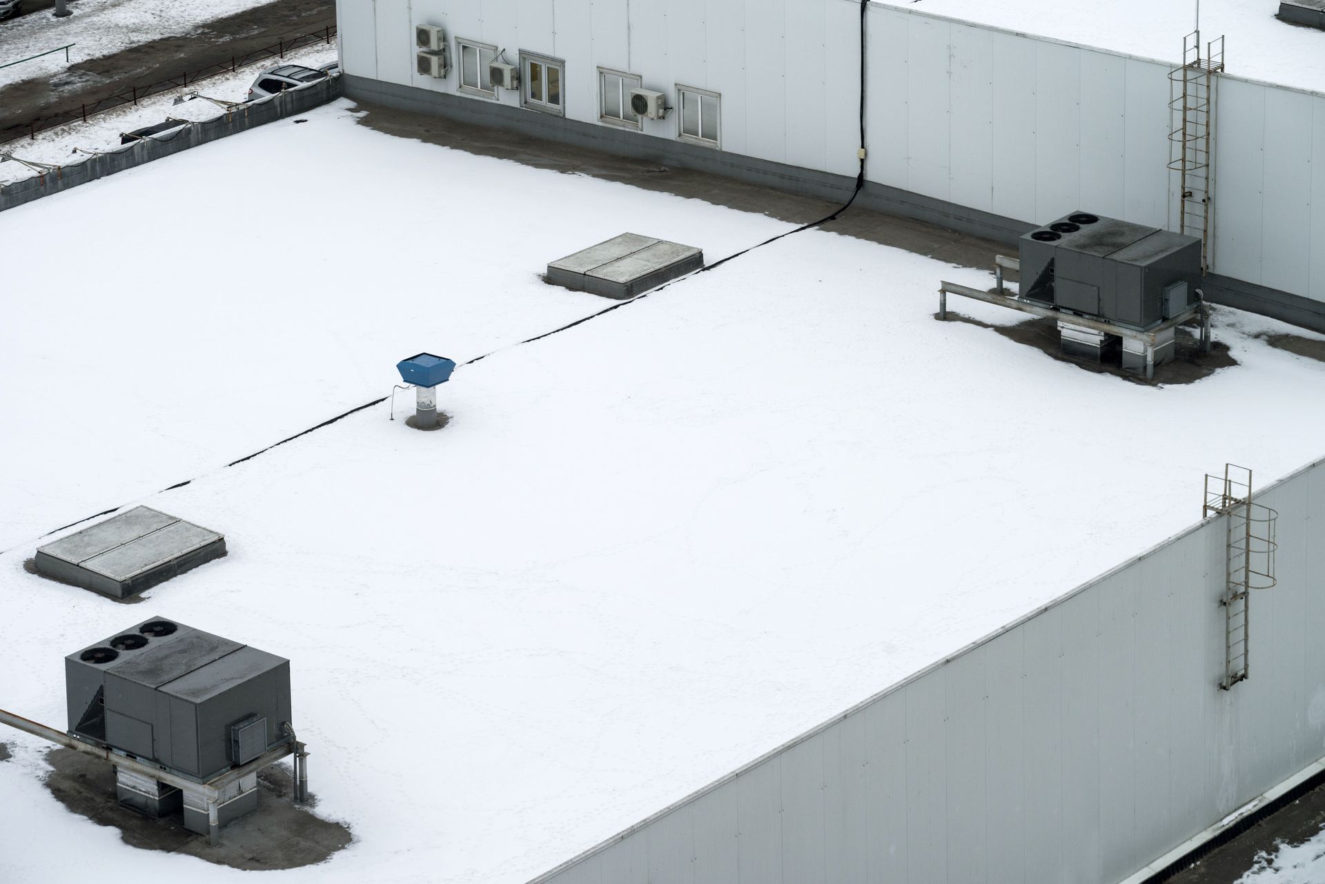 Snow-covered rooftop with HVAC units and vents on a white industrial building.