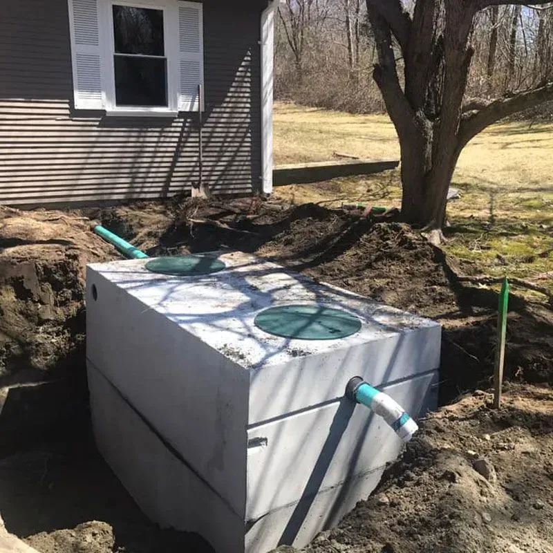 Septic tank installed beside a house, with green inspection covers and exposed pipes in a dirt excavation.