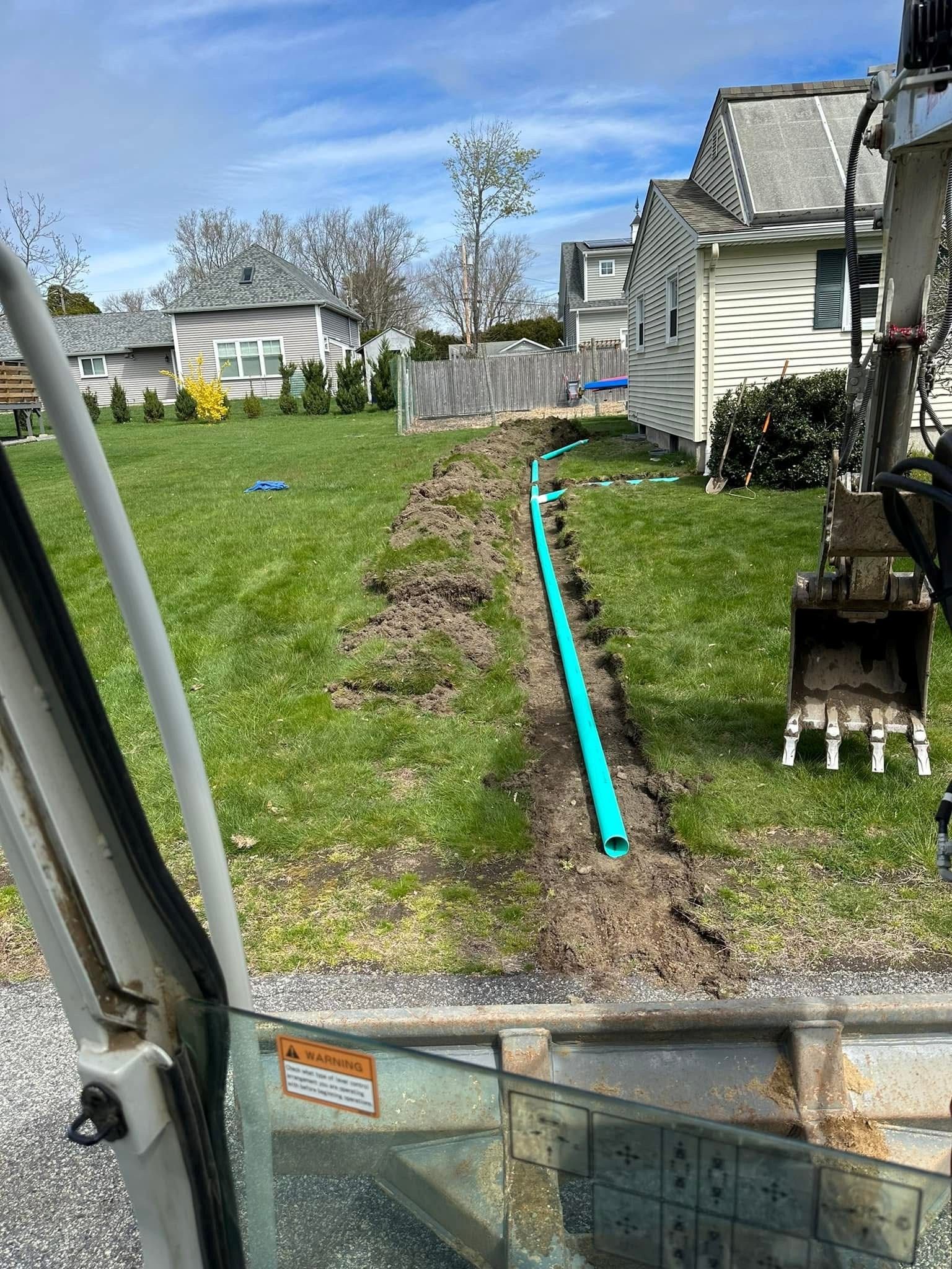 Backyard with a turquoise pipe along a dirt trench beside a house and lawn