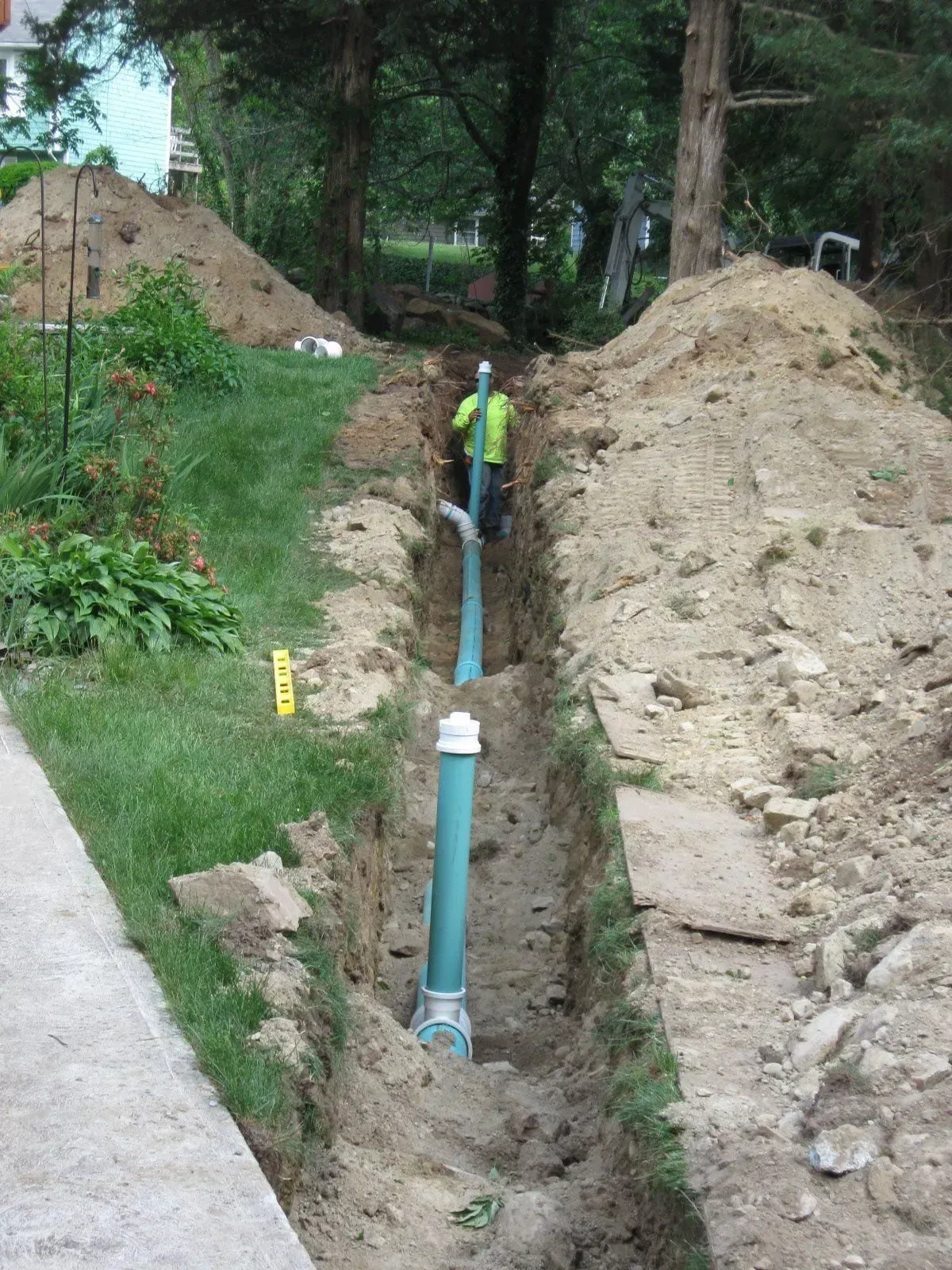 Worker in a trench installing a blue pipe beside dirt mounds at a construction site
