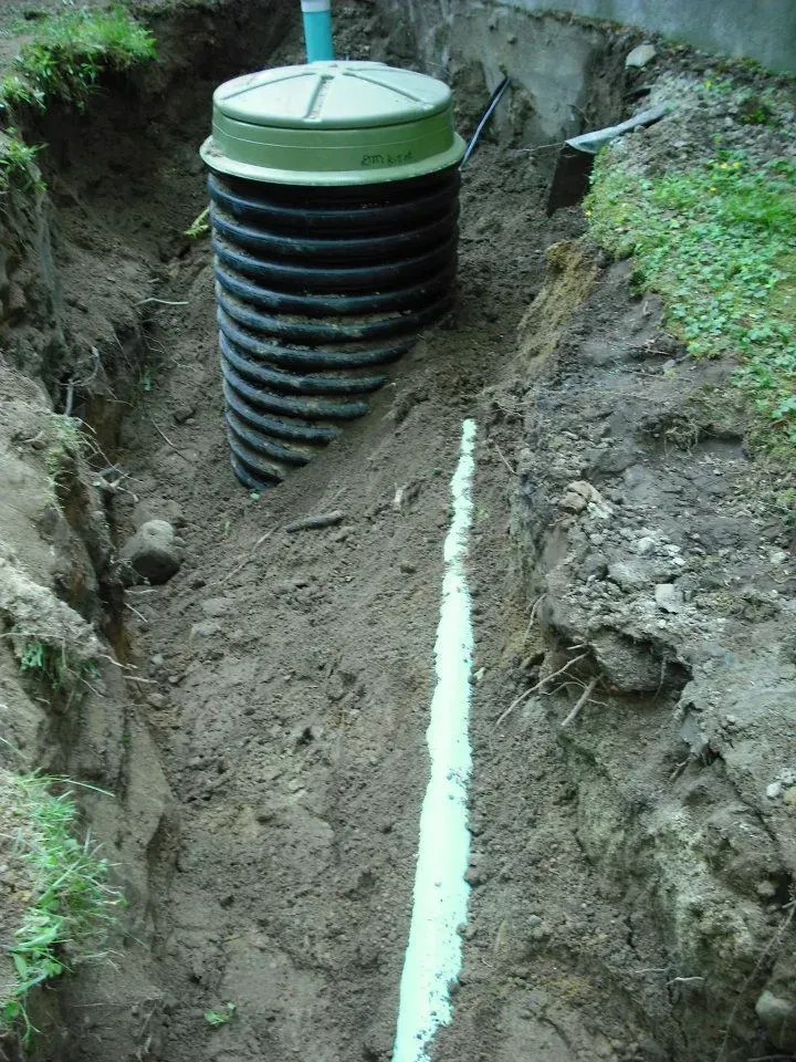 Black corrugated drainage pipe in a muddy trench with a green cap on top