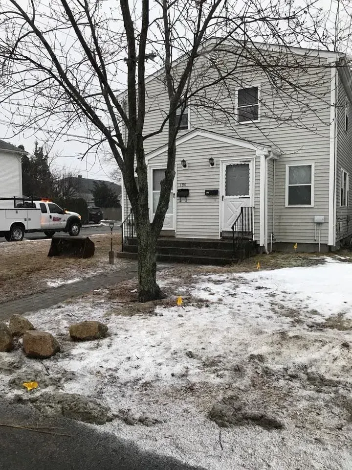 Snowy yard with a white house, leafless tree, and parked truck on a gray day