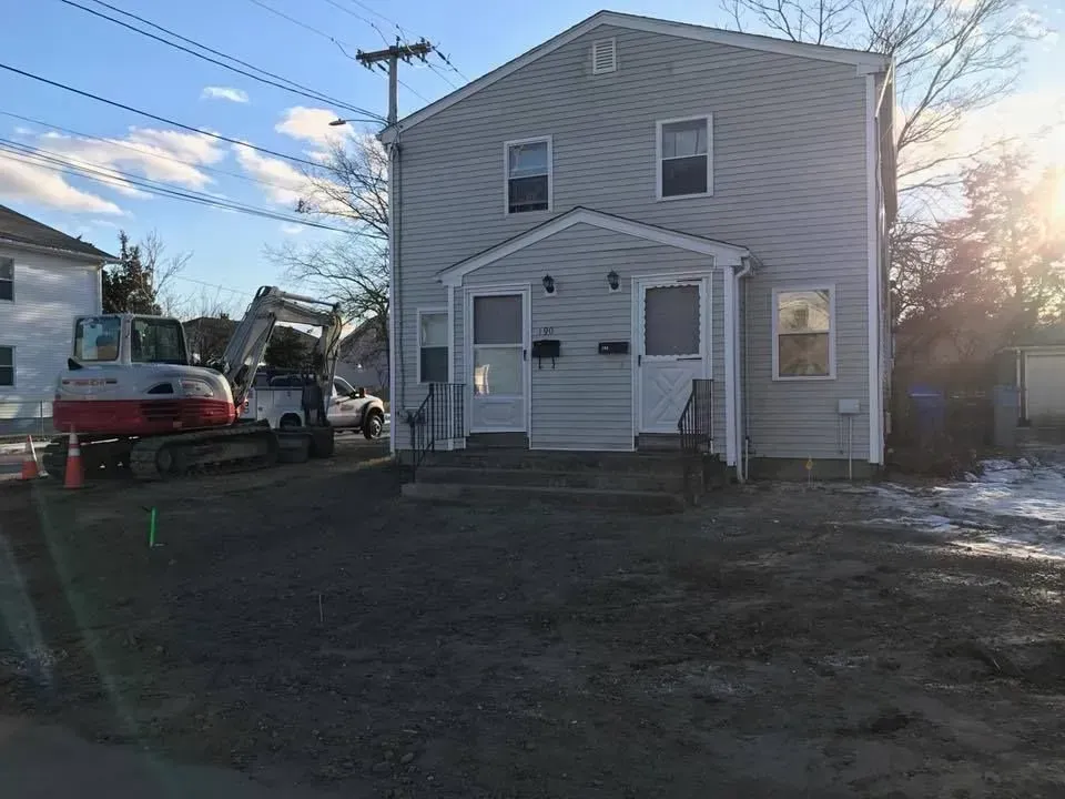 Two-story gray house with front porch and steps, a utility truck parked beside it at dusk