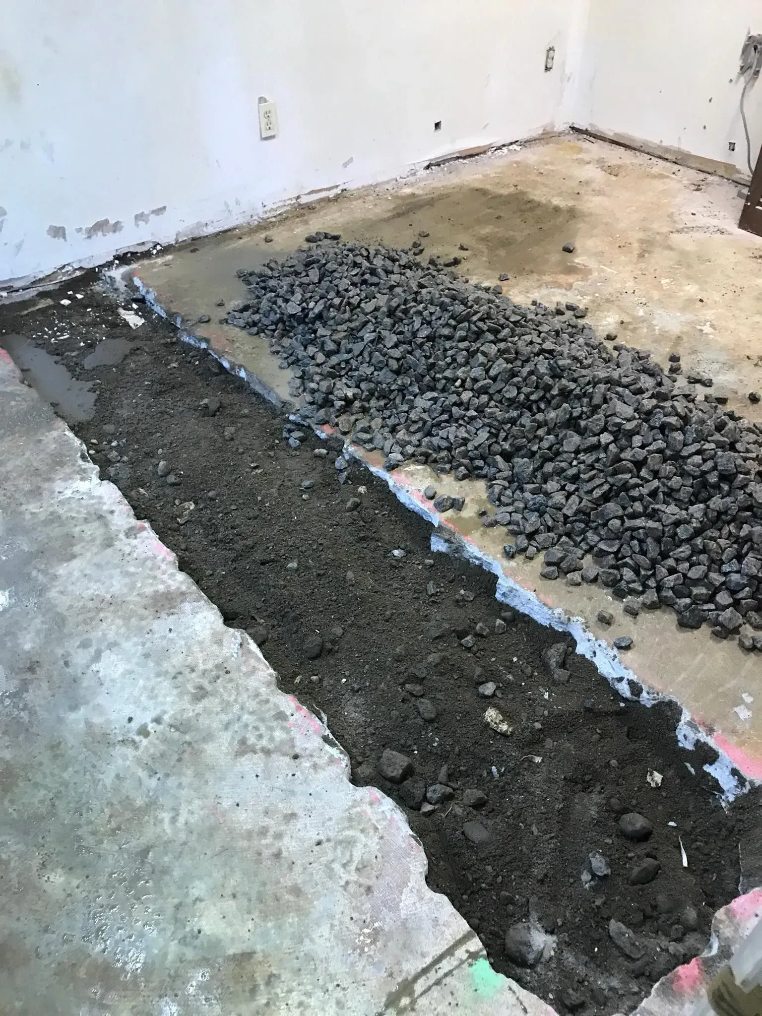 Partial floor demolition with exposed concrete and a pile of rubble in a bare room.
