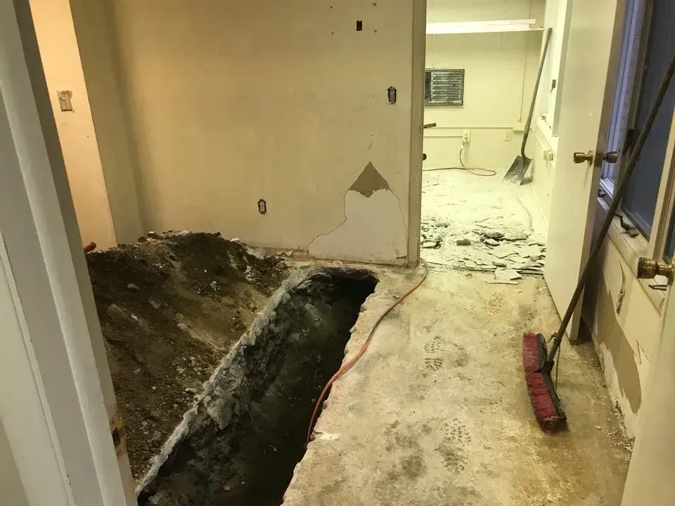 Damaged hallway with a large trench in the floor and scattered debris during renovation.