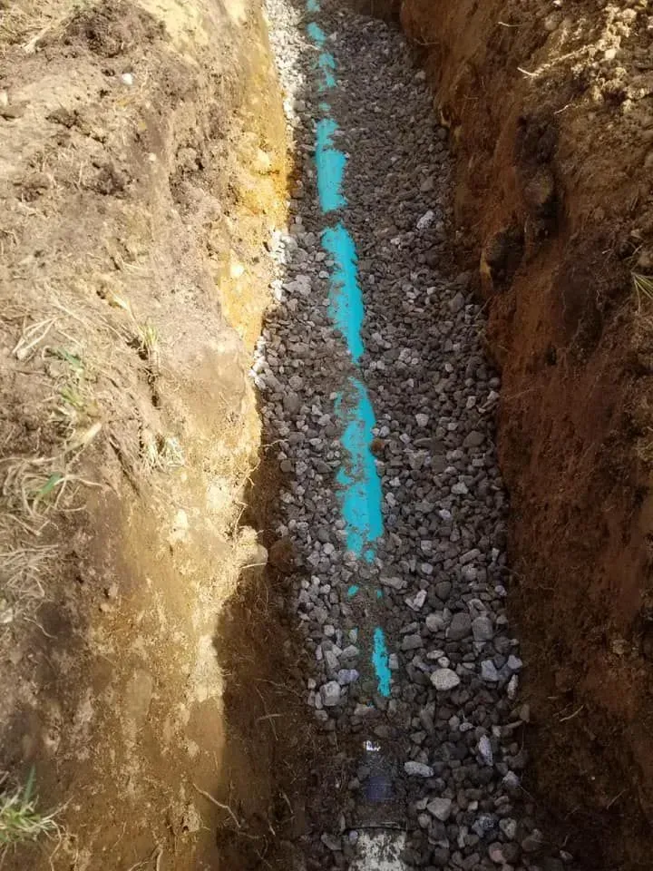 Narrow trench with gravel fill and a blue pipe running down the center
