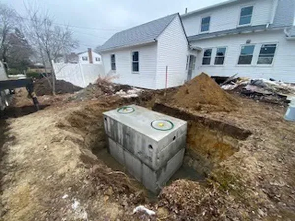 Backyard excavation exposing a concrete utility box beside a white house and muddy dirt piles