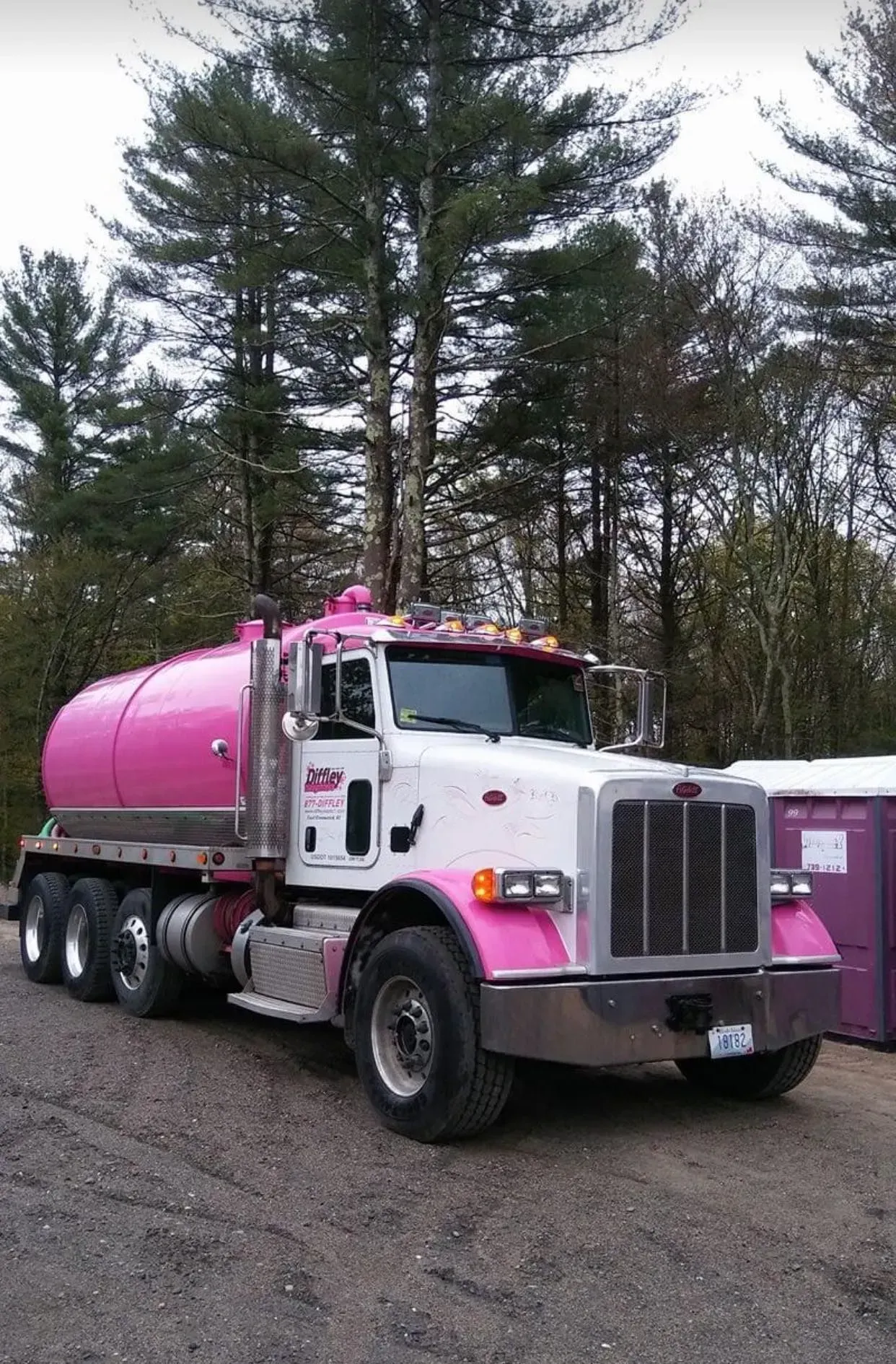 Pink cement mixer truck parked outdoors among trees and portable toilets