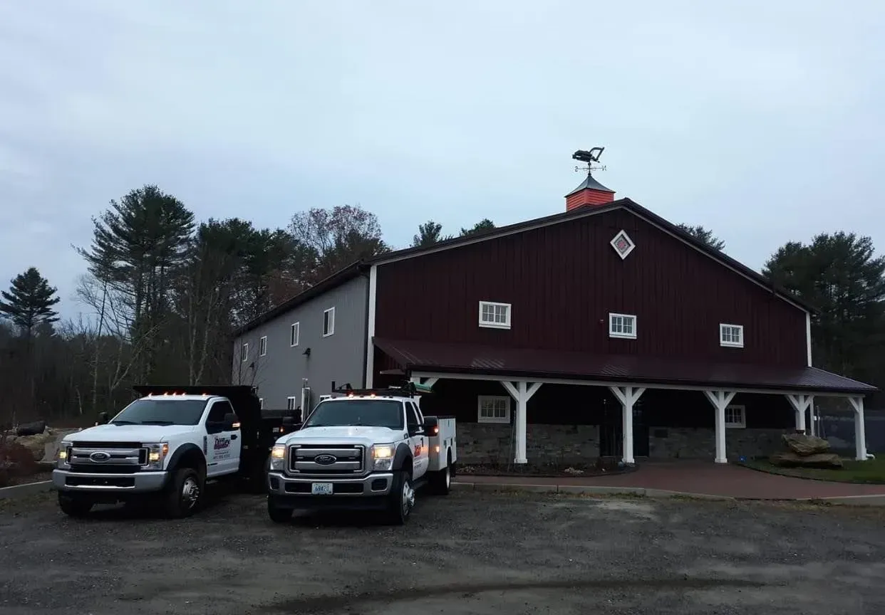 Two white pickup trucks parked in front of a red barn-like building at dusk
