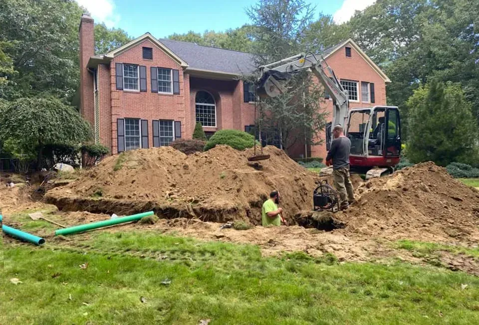 Workers and excavator digging a large dirt pile in front of a brick house