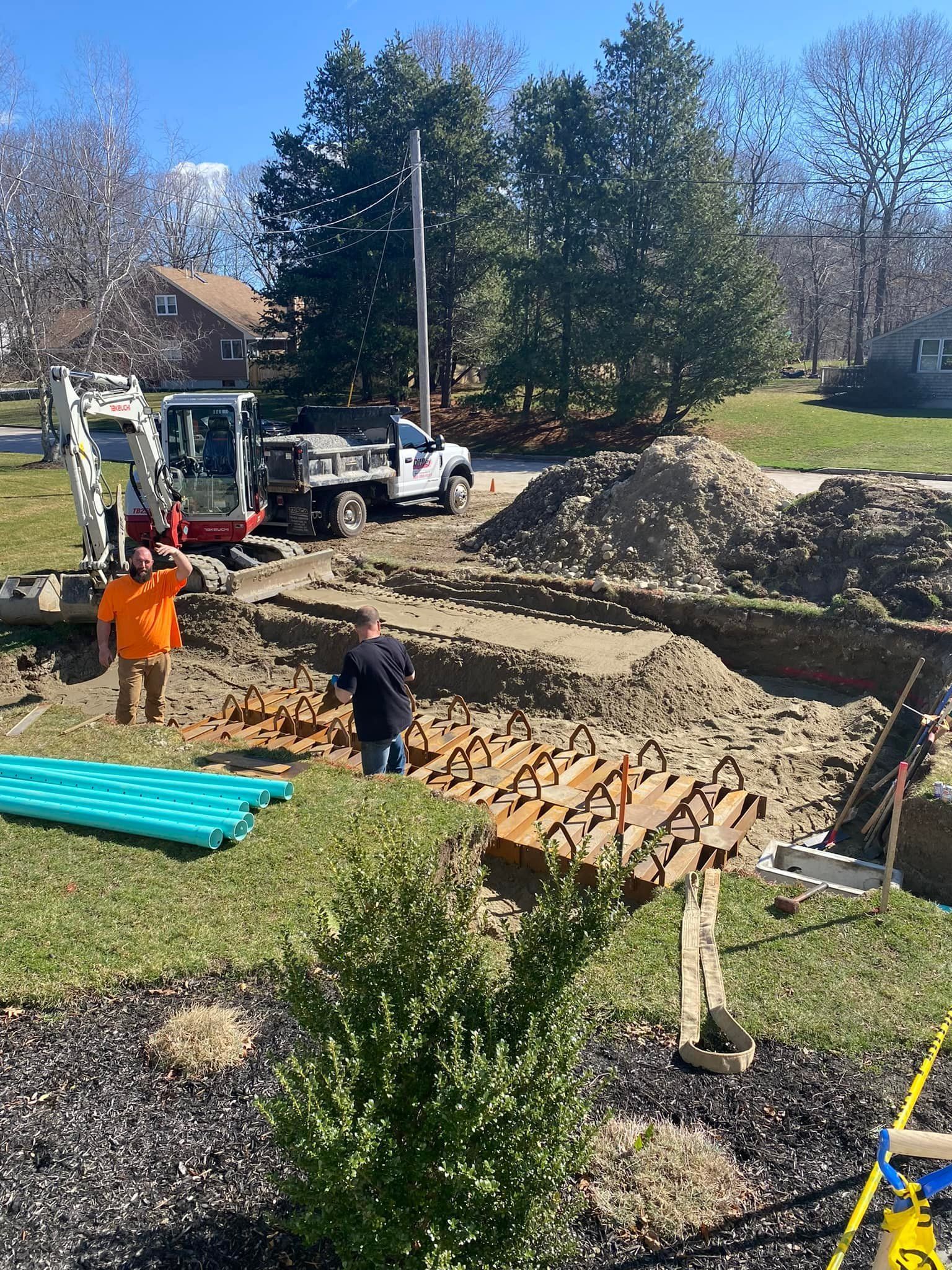 Workers and trucks at a construction site with dirt piles and stacked materials on a sunny day