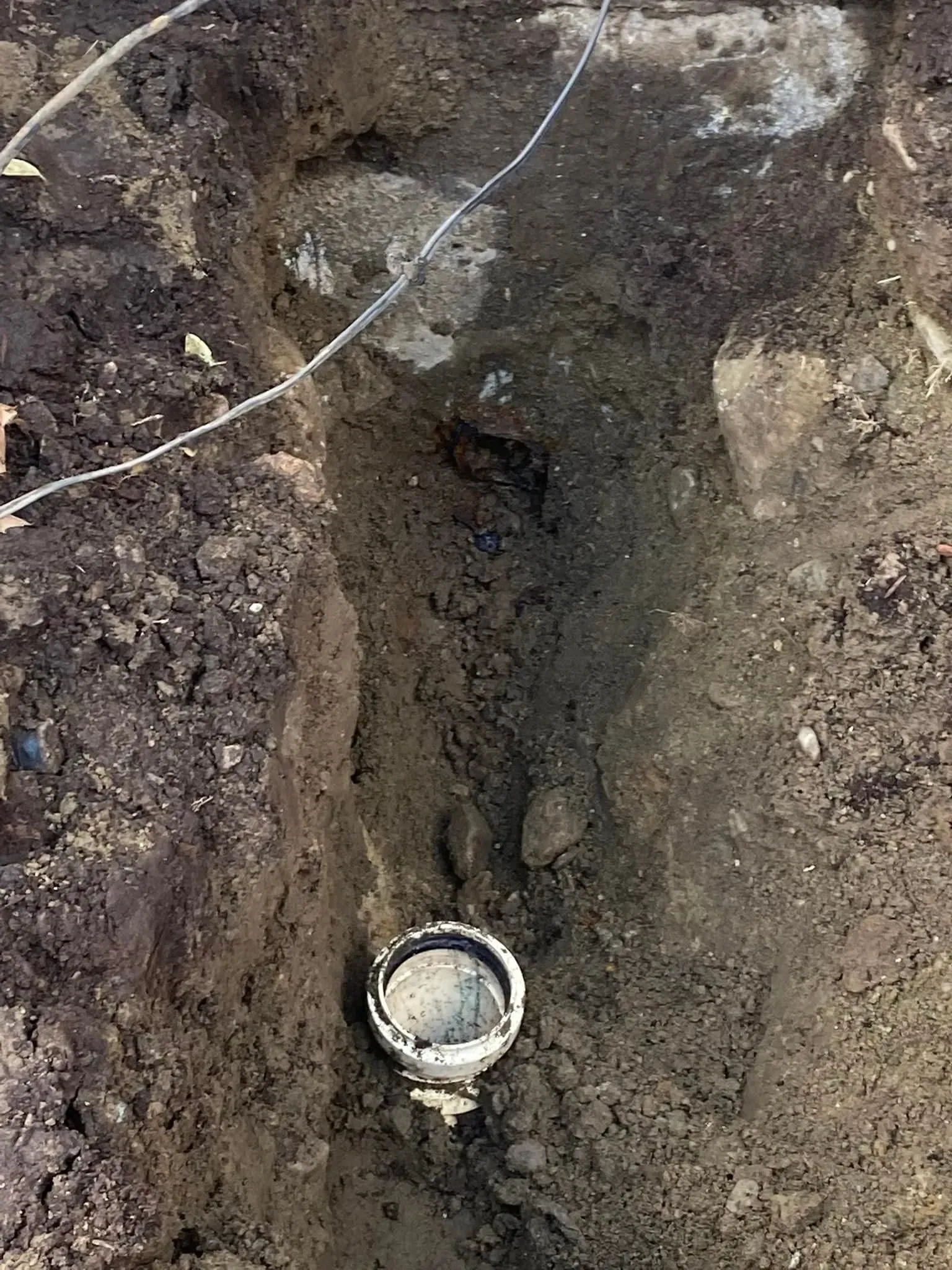 Small round pipe opening in a muddy dirt trench with a wire across the top.