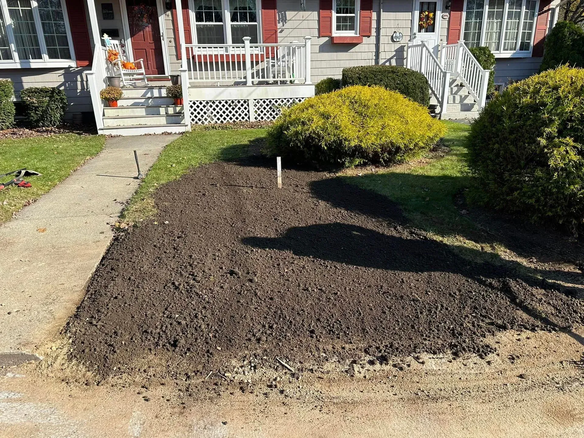 Freshly mulched front yard bed beside a sidewalk, in front of a house with porch steps.