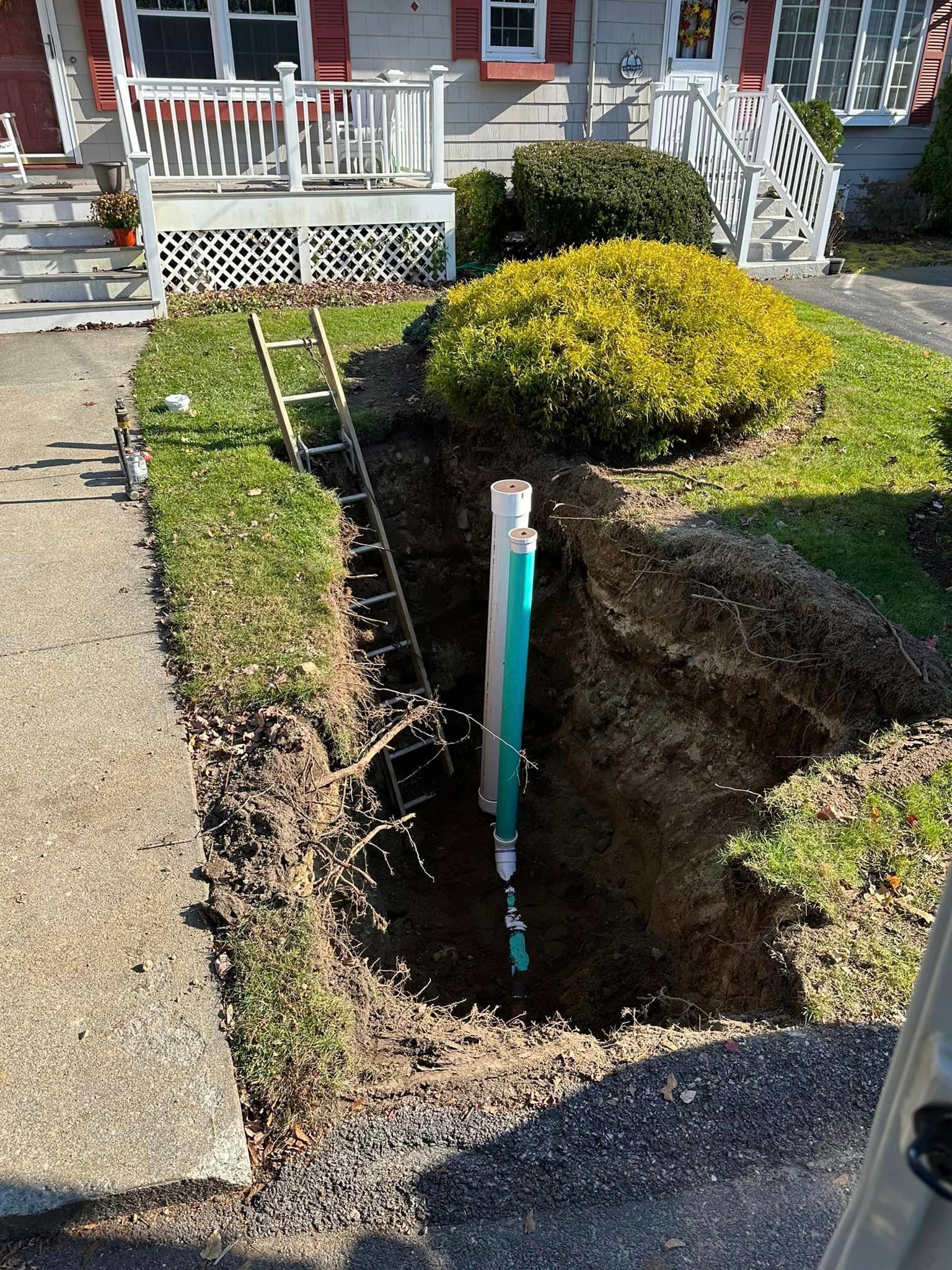 Open trench beside a walkway with a teal utility stake and hose near a house porch and bushes