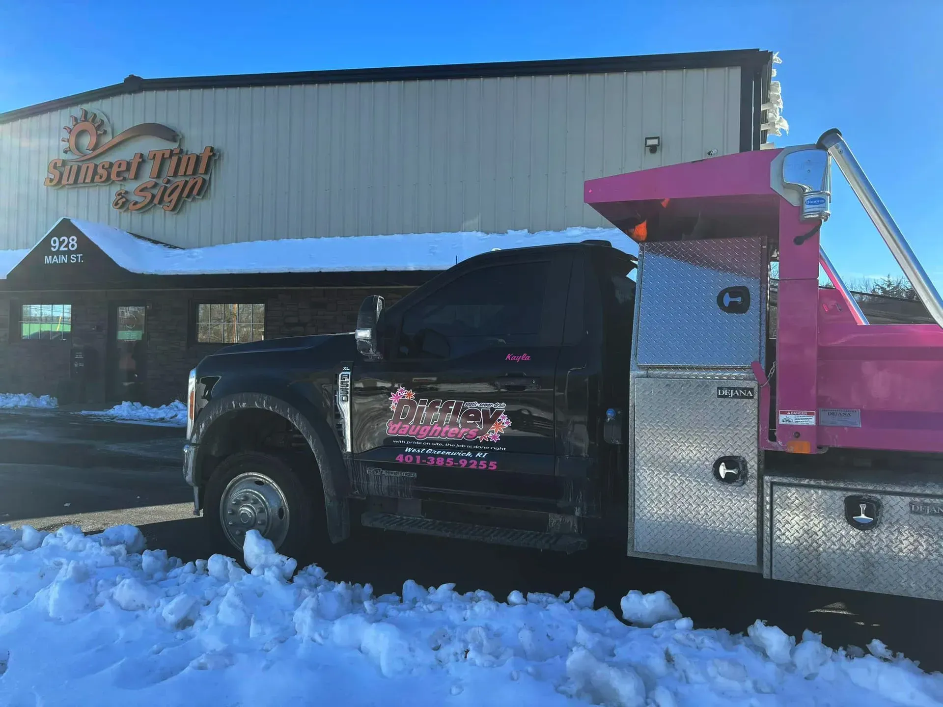 Pink-and-black tow truck parked in front of a restaurant in snowy daylight
