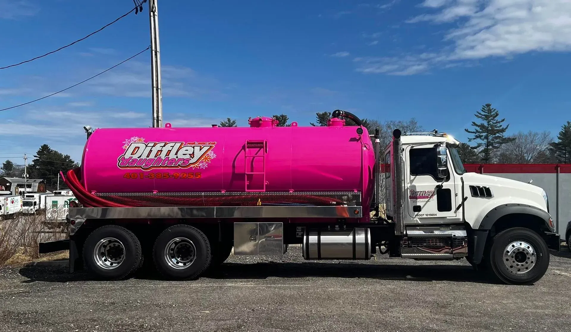 White tanker truck with bright pink tank parked outdoors on a sunny day