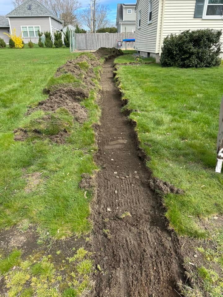 Dug trench through a grassy backyard beside a house, with piles of dirt on one side.