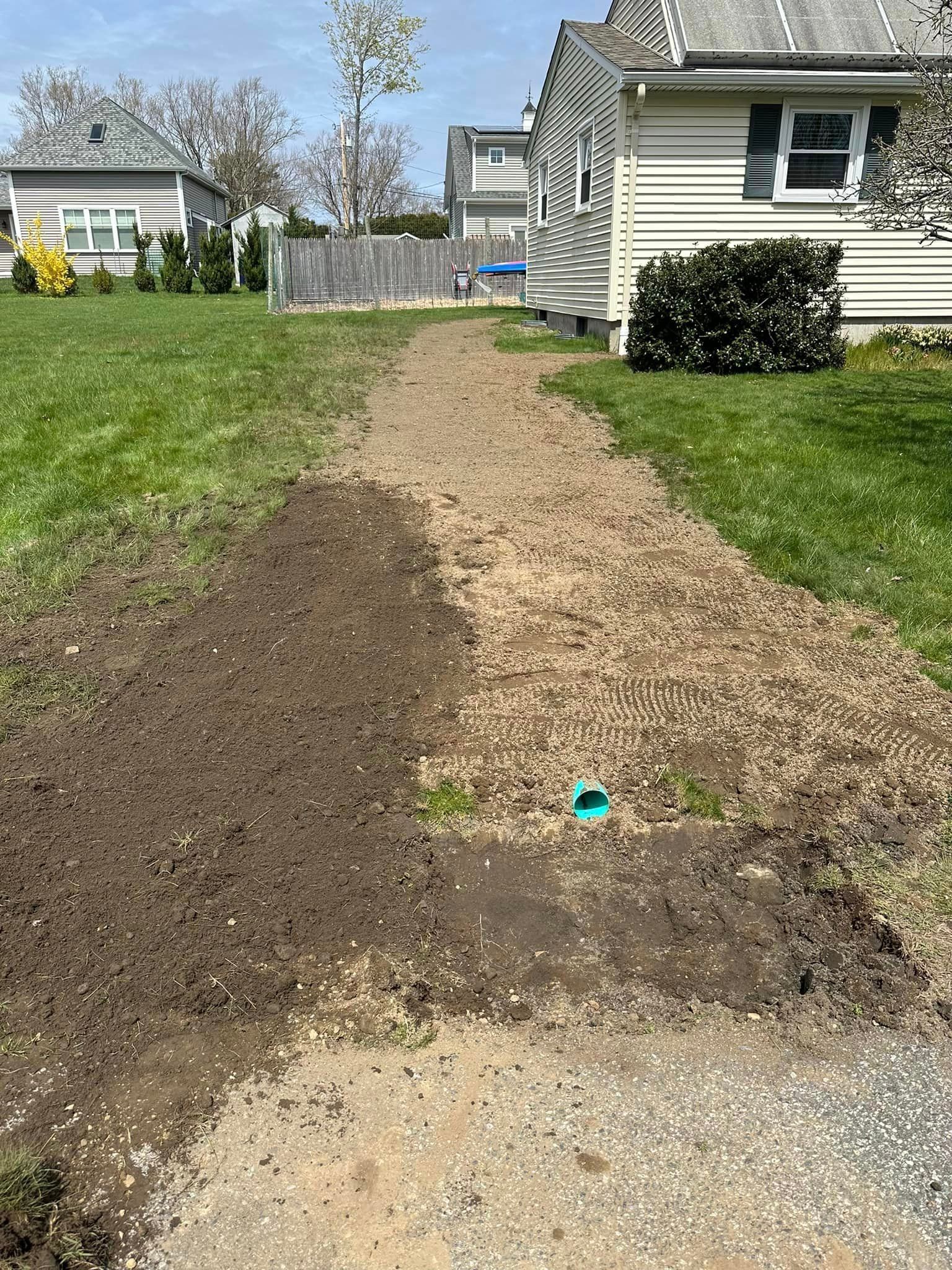 Gravel path under construction beside a house, bordered by dirt and grass with a small blue marker.