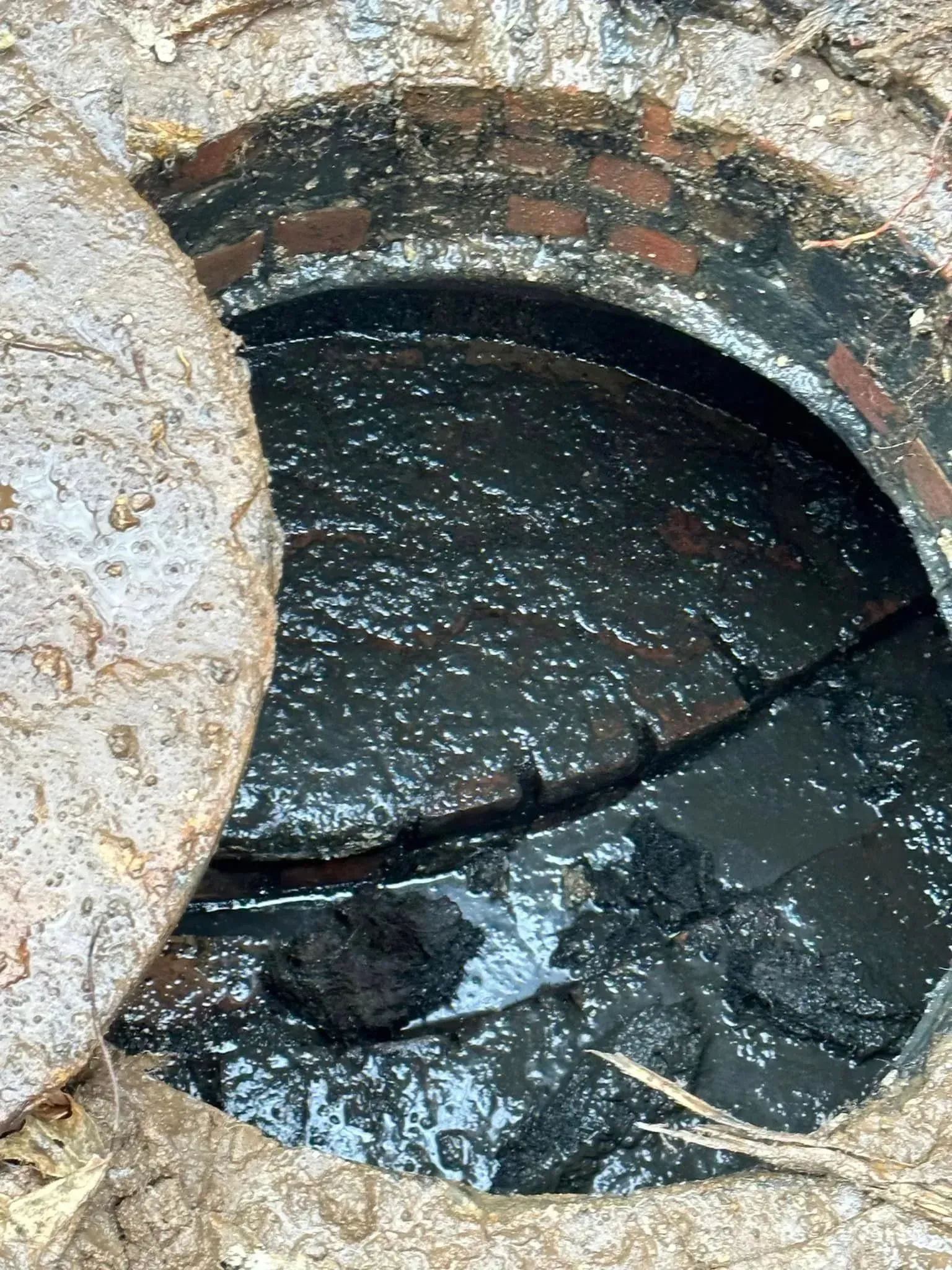Open brick manhole with dirty standing water and debris inside